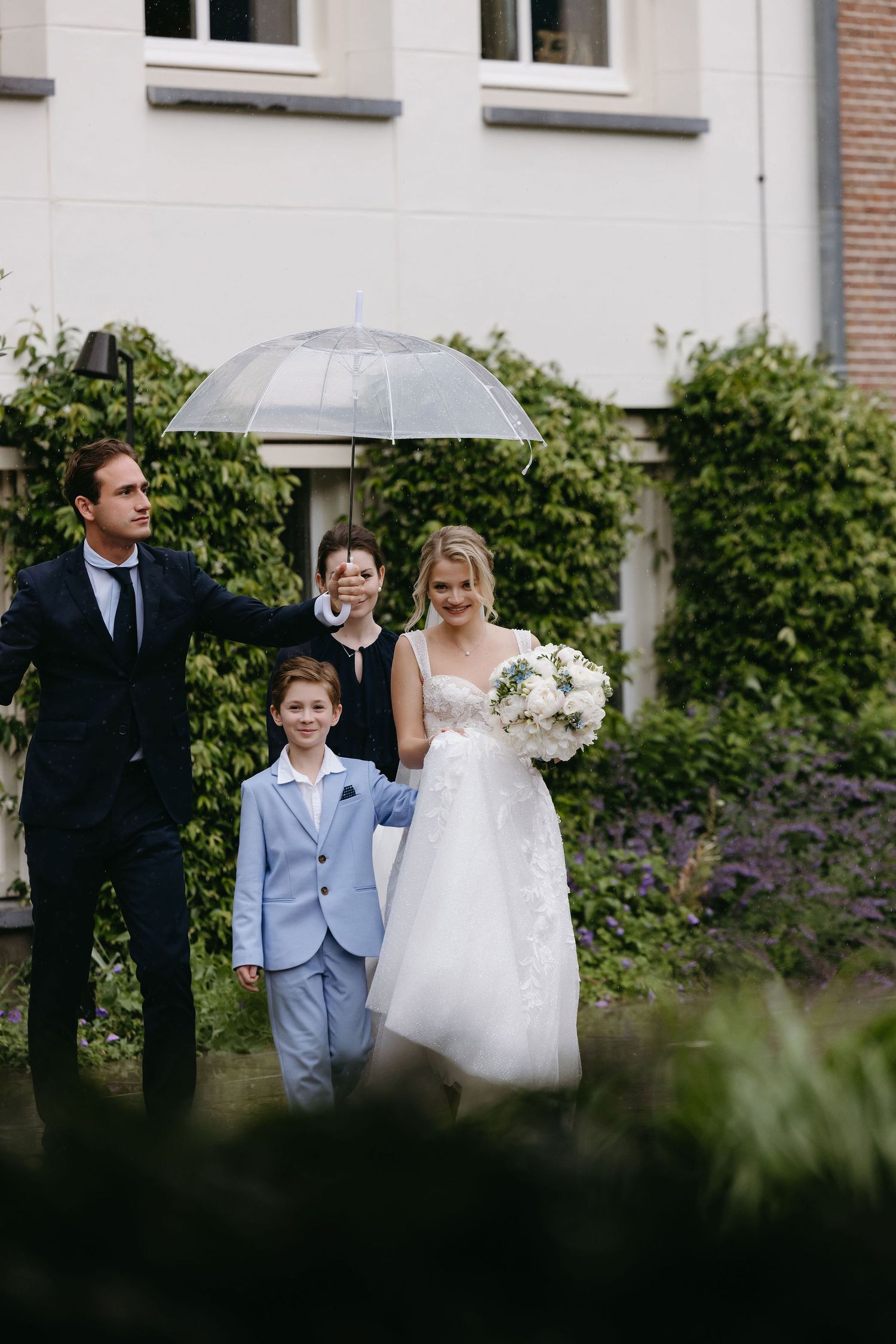 Wedding party gathering outside a white building with brick accents.