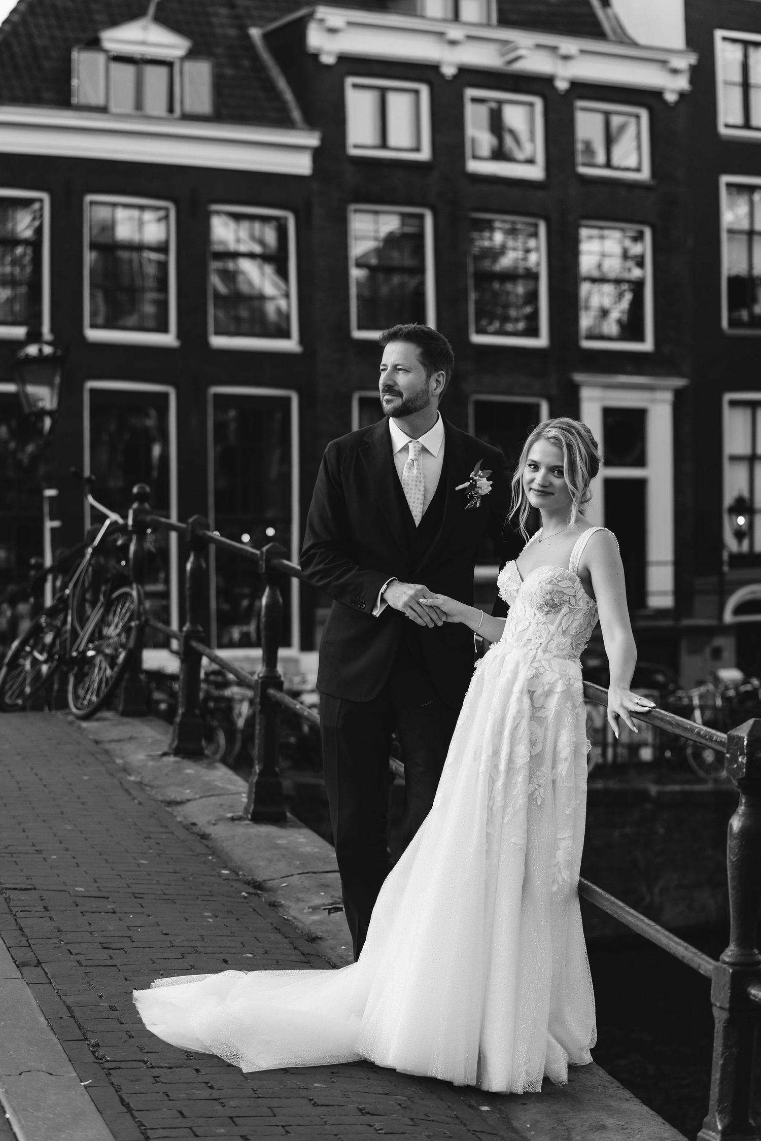 Couple walking along Amsterdam canal street with bride's dress flowing in wind.