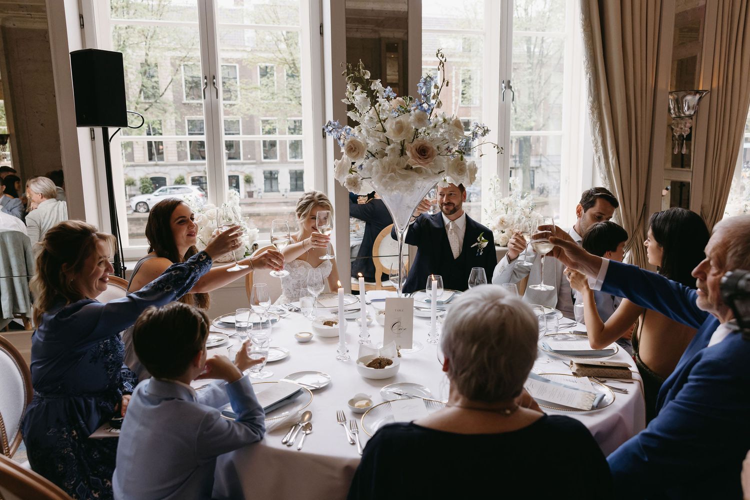 Wedding reception dining room with large windows and guests seated at decorated tables.