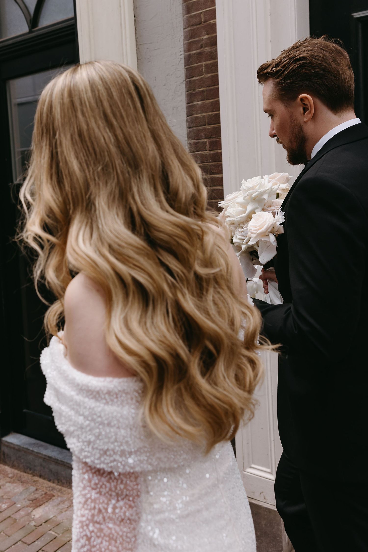 Elegant couple in wedding attire photographed from behind showing flowing hair and formal details.