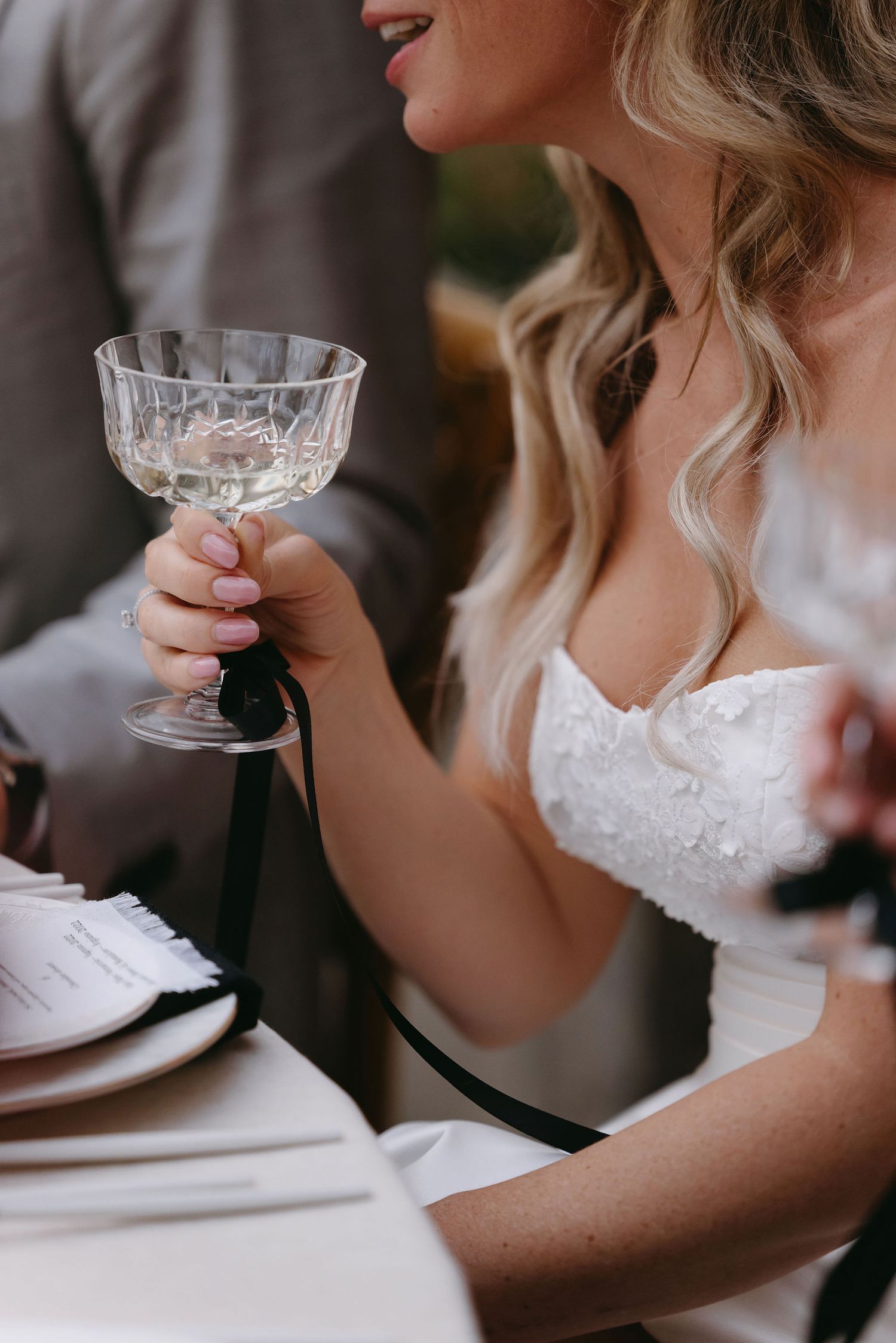 A close-up shot of someone in a white wedding dress holding a crystal champagne glass.