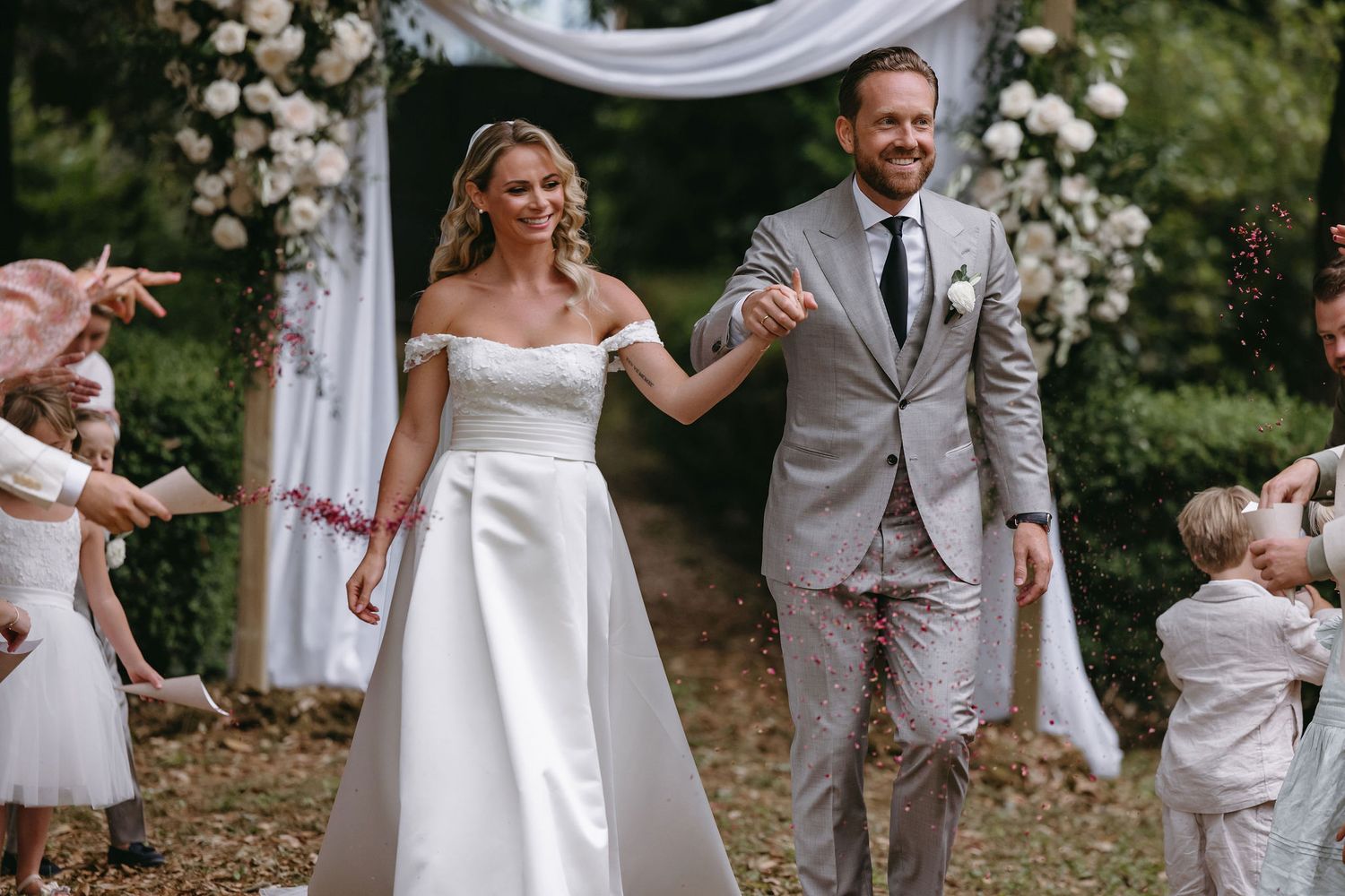 A lovely outdoor wedding ceremony with decorative white fabric draping and floral arrangements in a garden setting.