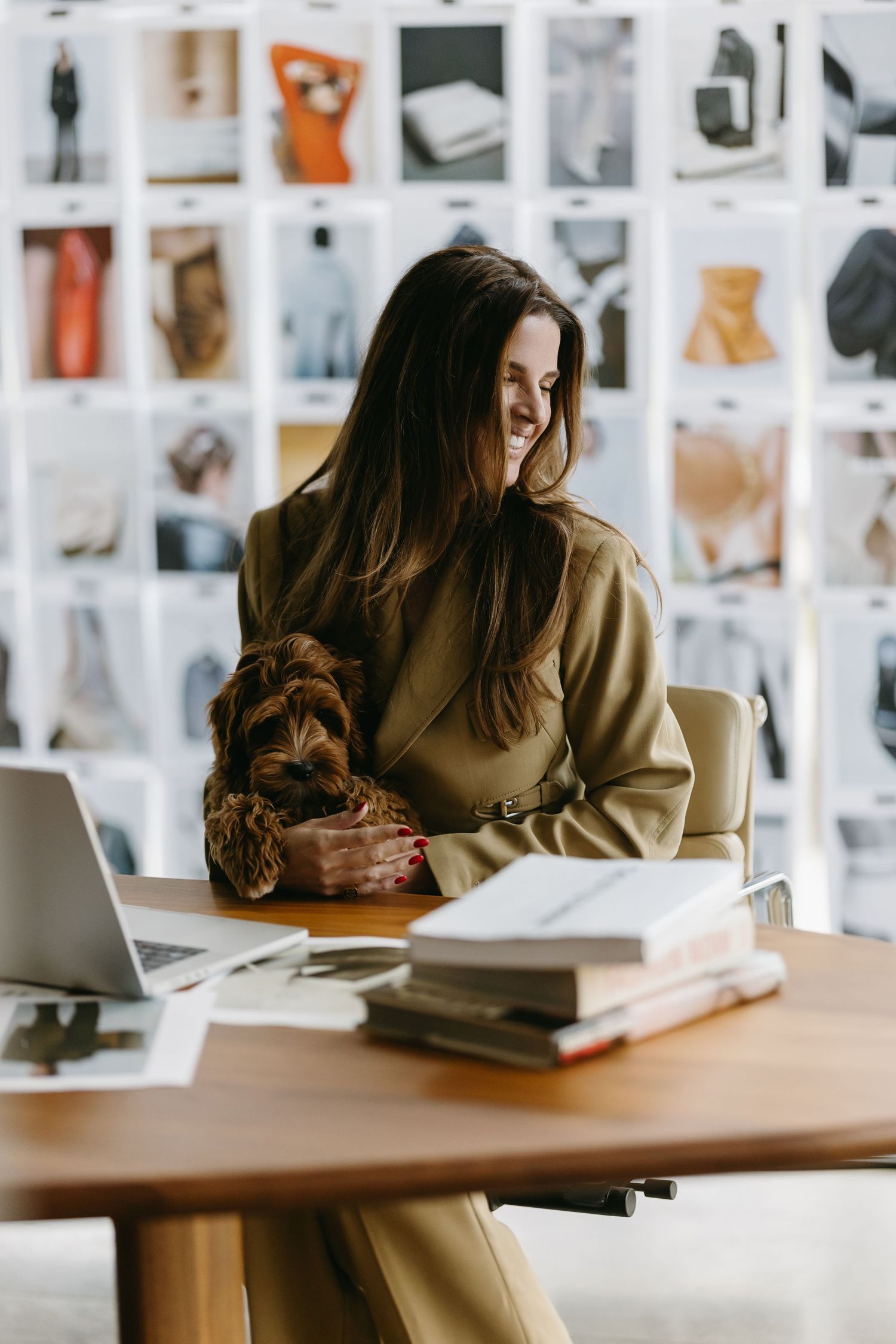 Person working at desk with laptop and mood board while petting small dog.