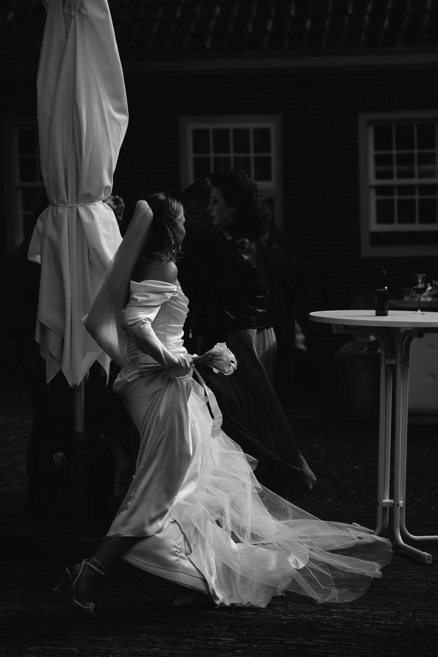 Black and white photo of dancing couple under patio umbrella at nighttime wedding reception.