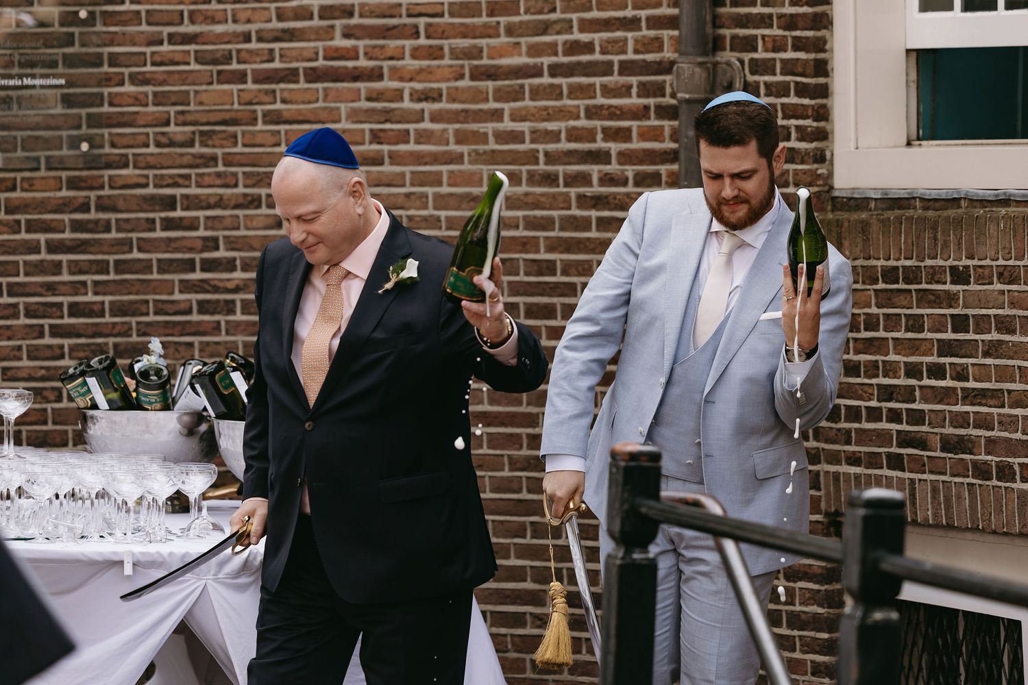 Wedding guests in formal attire gather on a brick patio for traditional Jewish ceremony festivities.