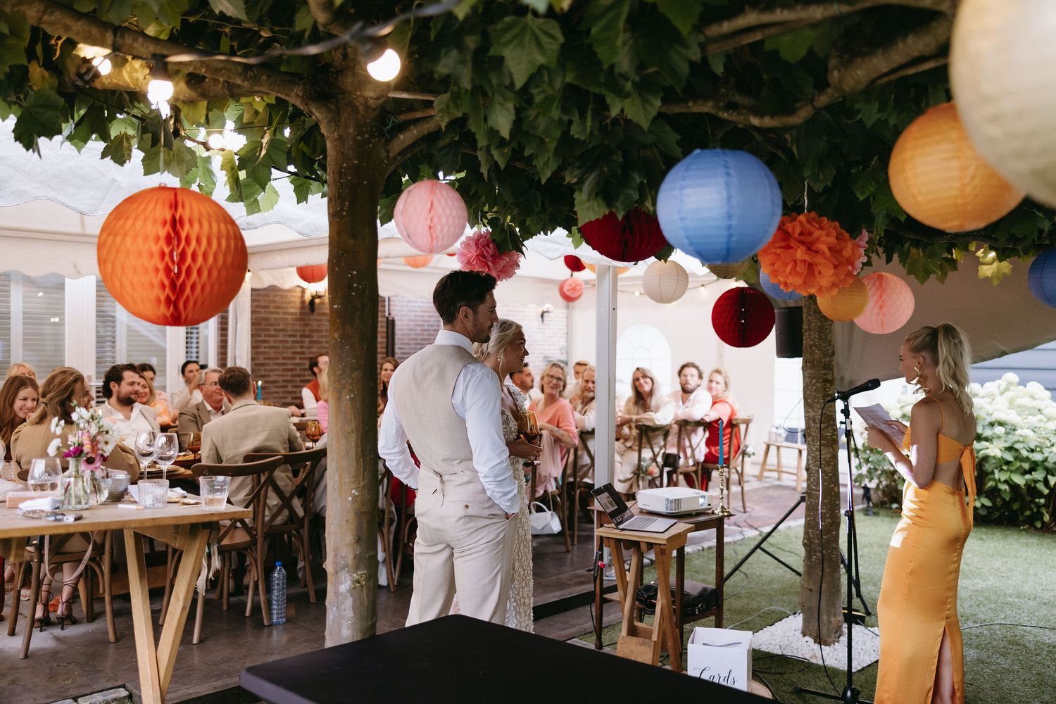 Outdoor wedding reception decorated with hanging paper lanterns and string lights.