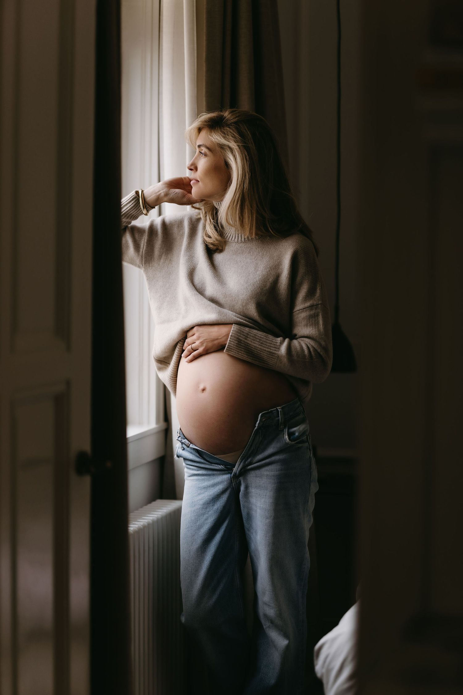 Moody maternity photos captured in natural window light with a grey sweater.
