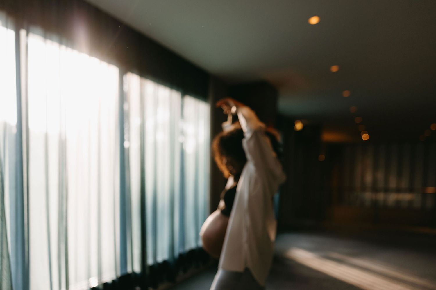 Silhouette figure stands near sunlit curtains in a moody indoor corridor.