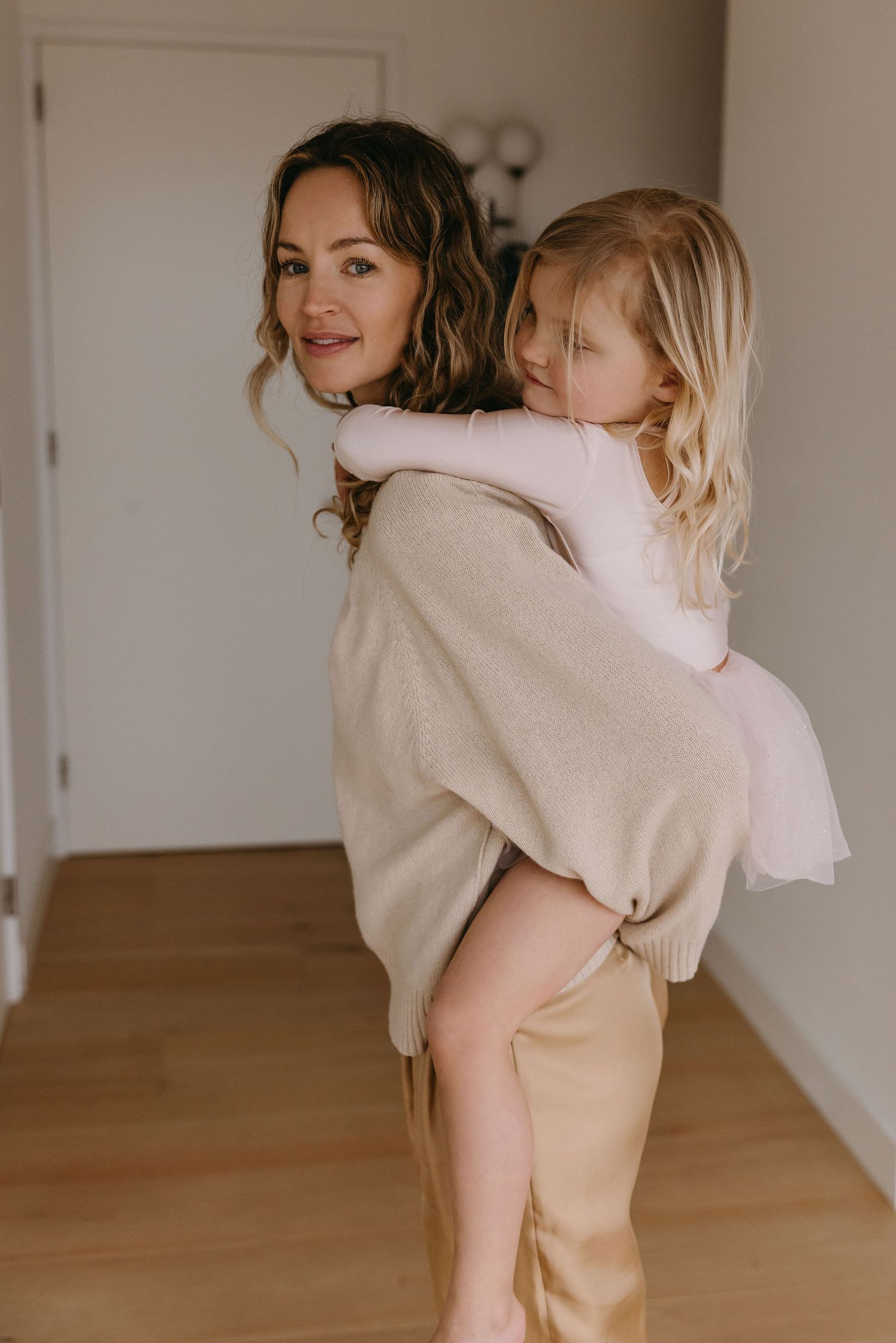 Parent giving piggyback ride to child in neutral-toned home setting.