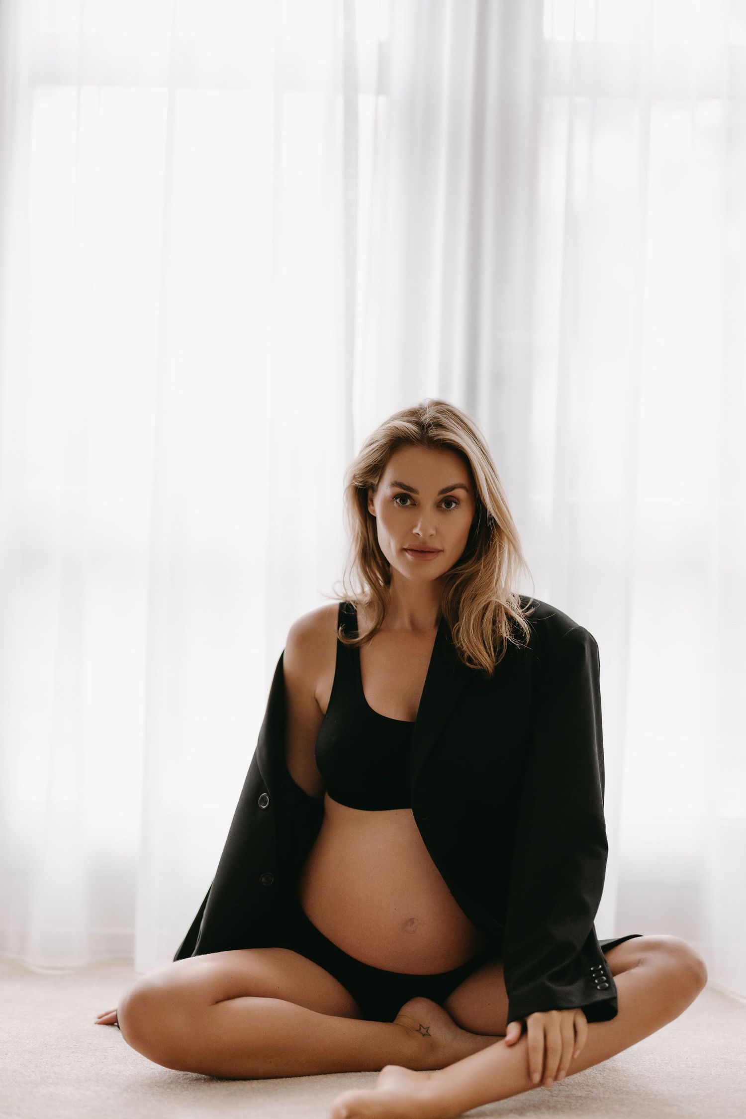 Minimalist maternity portrait against bright white curtains in black outfit.