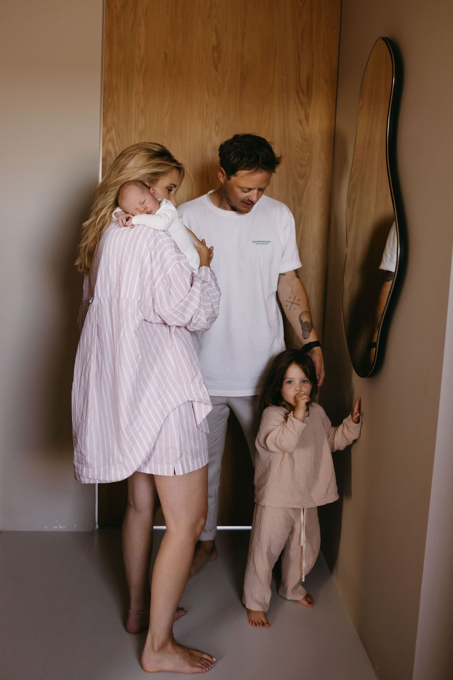 A family standing together in casual attire against a wooden wall with a decorative mirror.