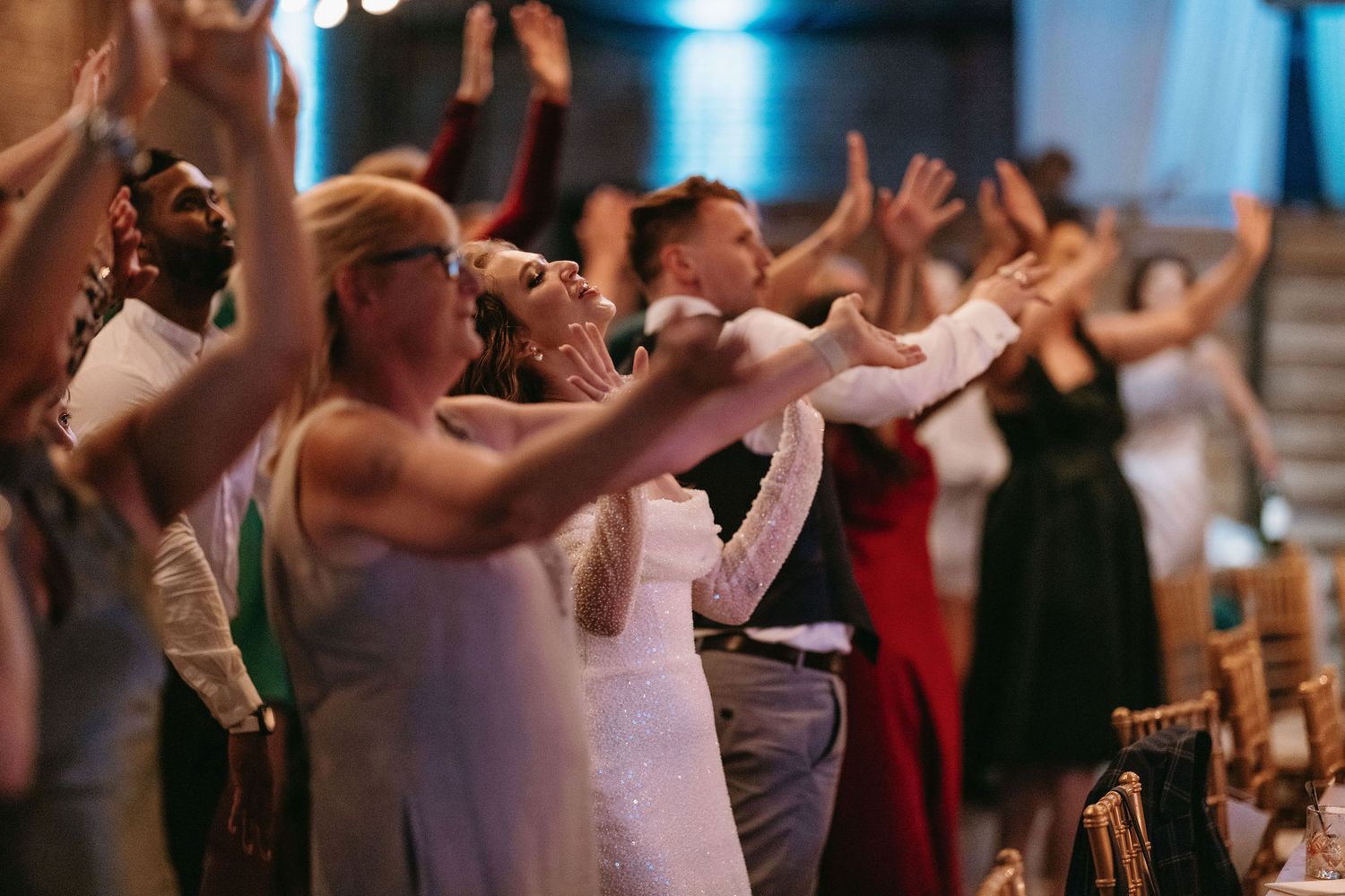 Wedding guests enjoying a lively dance party on a dim-lit dance floor with hanging lights.