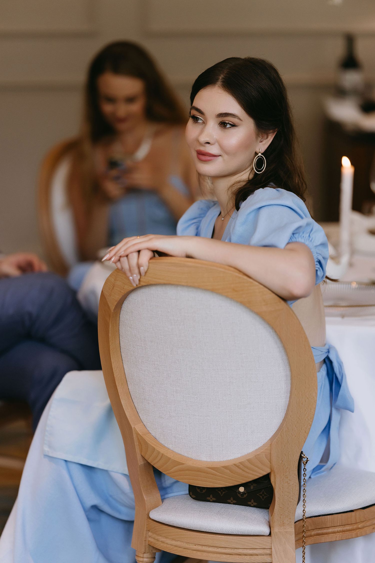 Wedding guest in light blue dress seated in elegant upholstered dining chair.