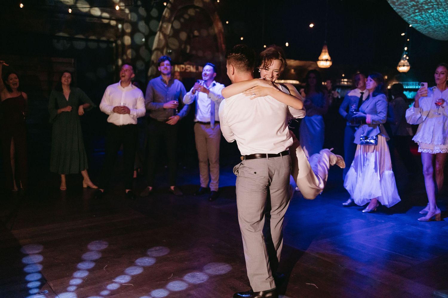 Couples dancing on a dimly lit dance floor with blue lighting at a wedding reception.