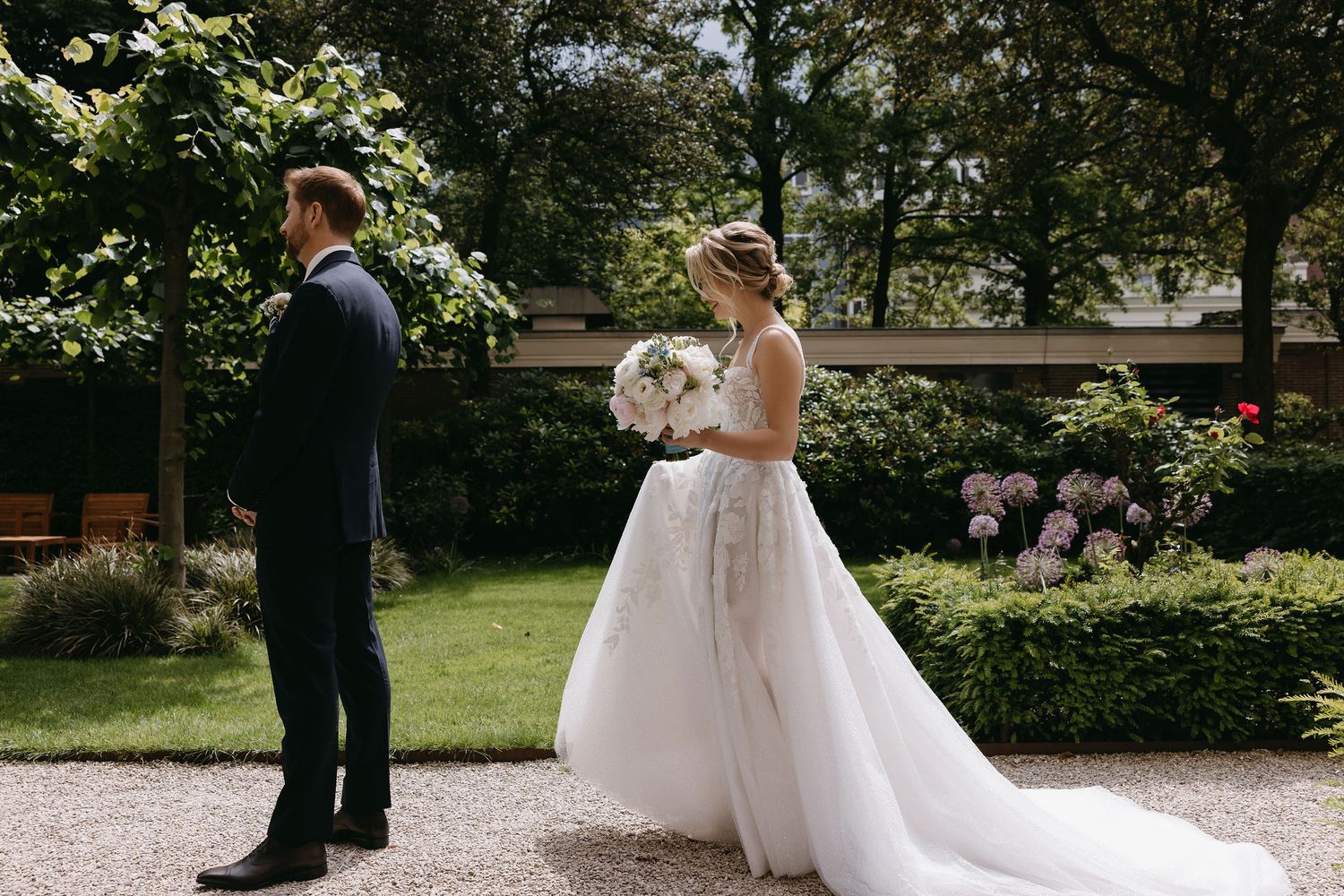 First look moment between bride and groom on garden path surrounded by greenery.