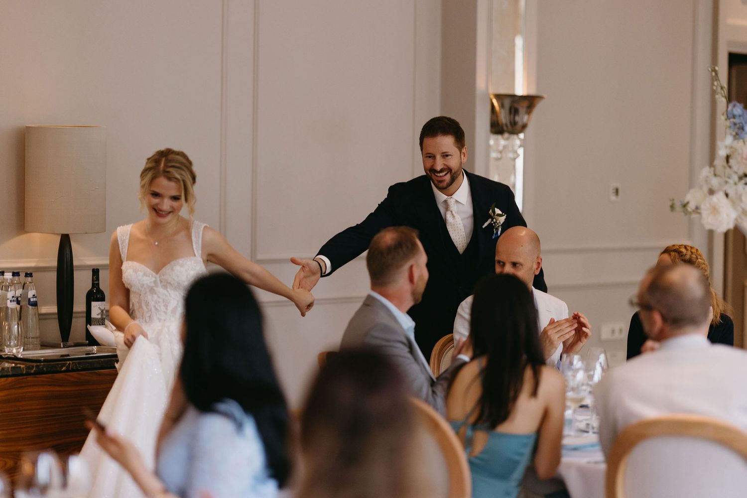 Wedding reception scene with guests seated at tables watching a celebratory moment.