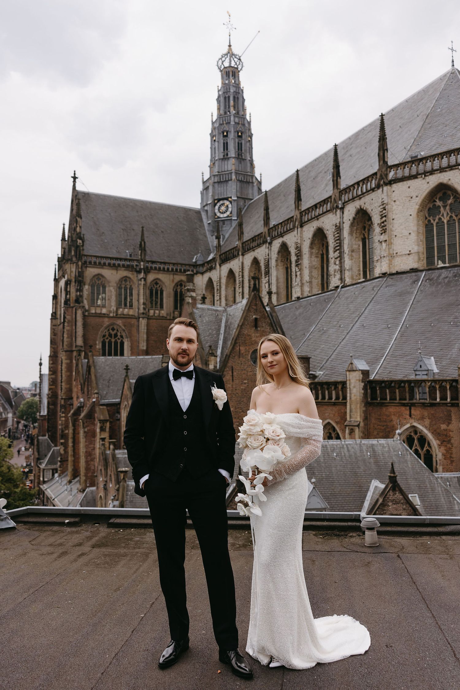 Wedding couple poses in front of majestic Gothic cathedral with ornate spires and architecture.