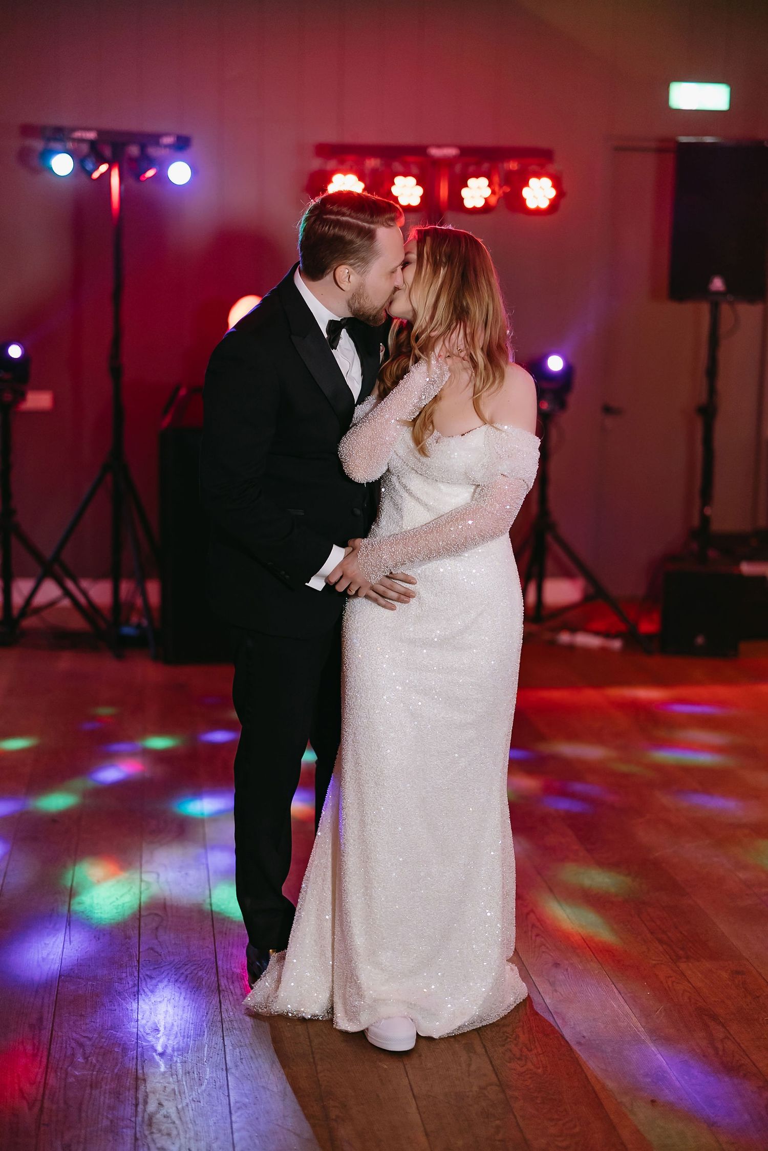 A couple shares their first dance together on a dance floor illuminated by colorful disco lights.