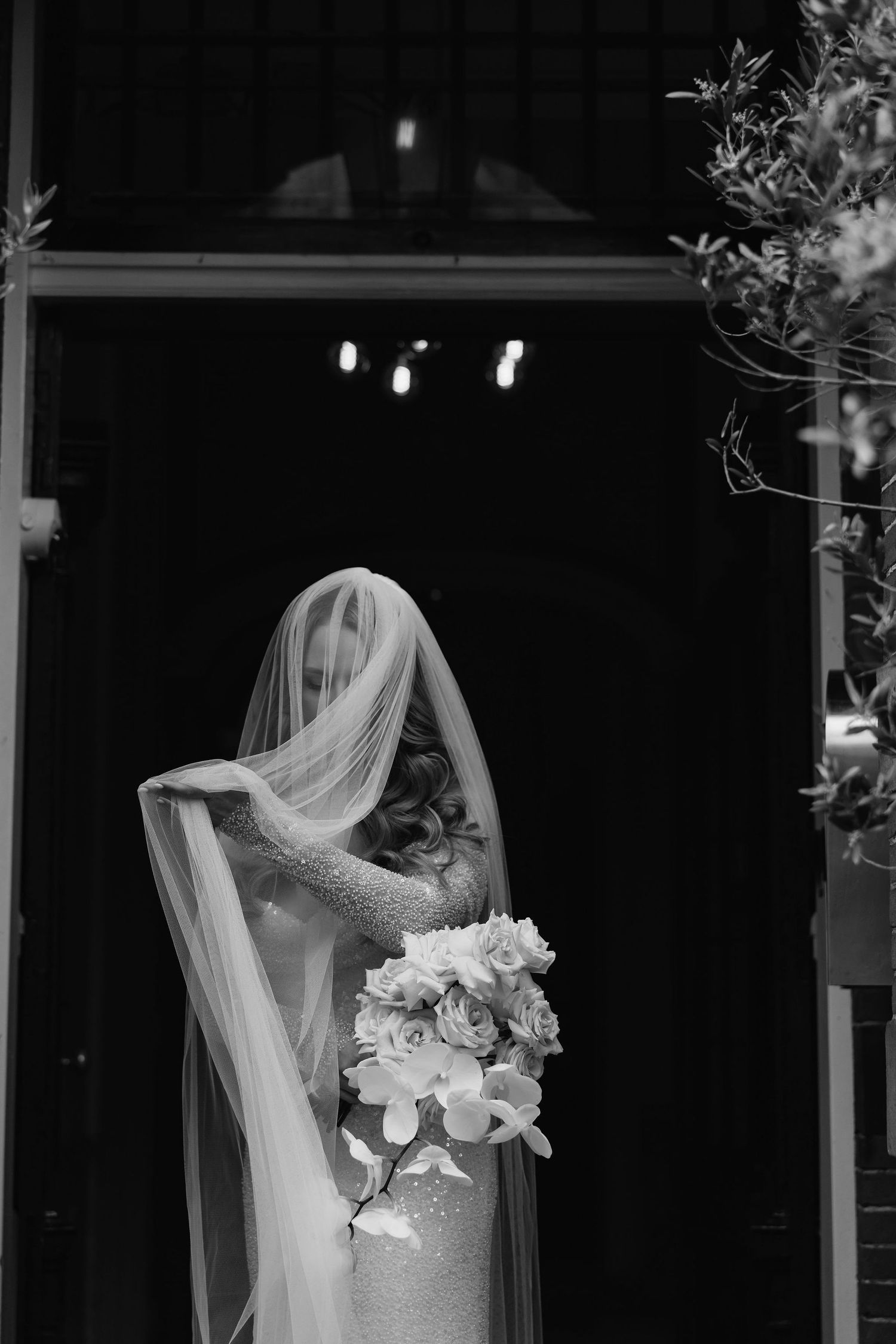 Bride in white dress and veil standing in doorway with delicate floral details.