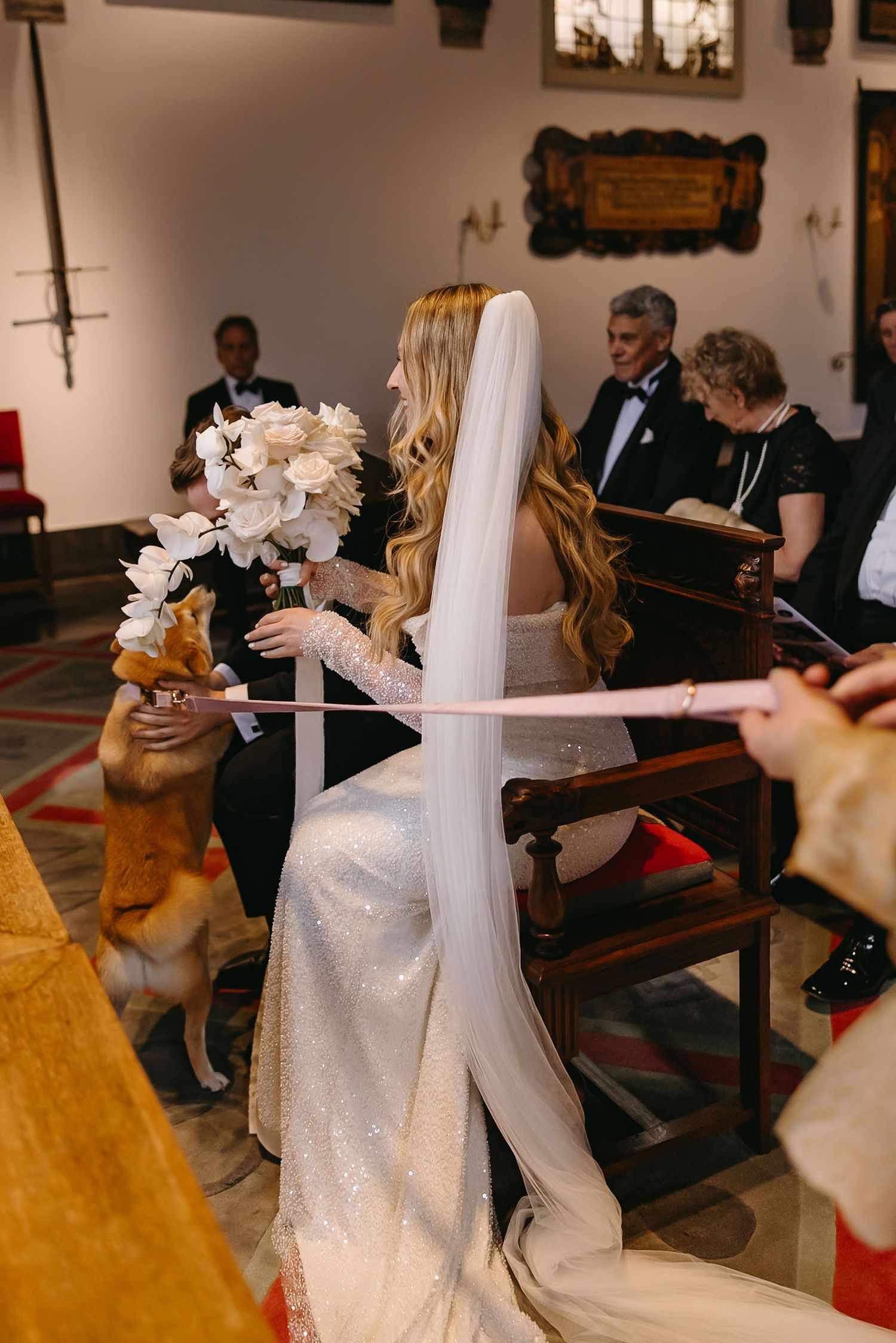 A bride in a white gown with a dog during a church ceremony.