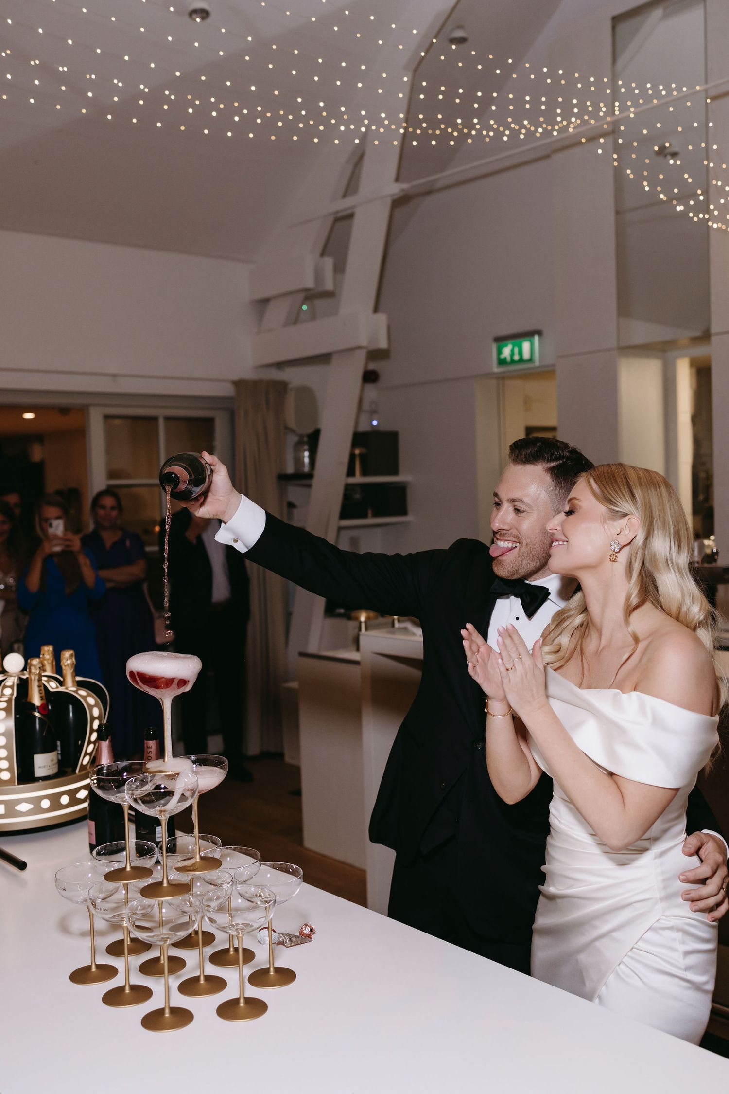 Couple celebrating at an elegant event with champagne tower and fairy lights decorating the ceiling.