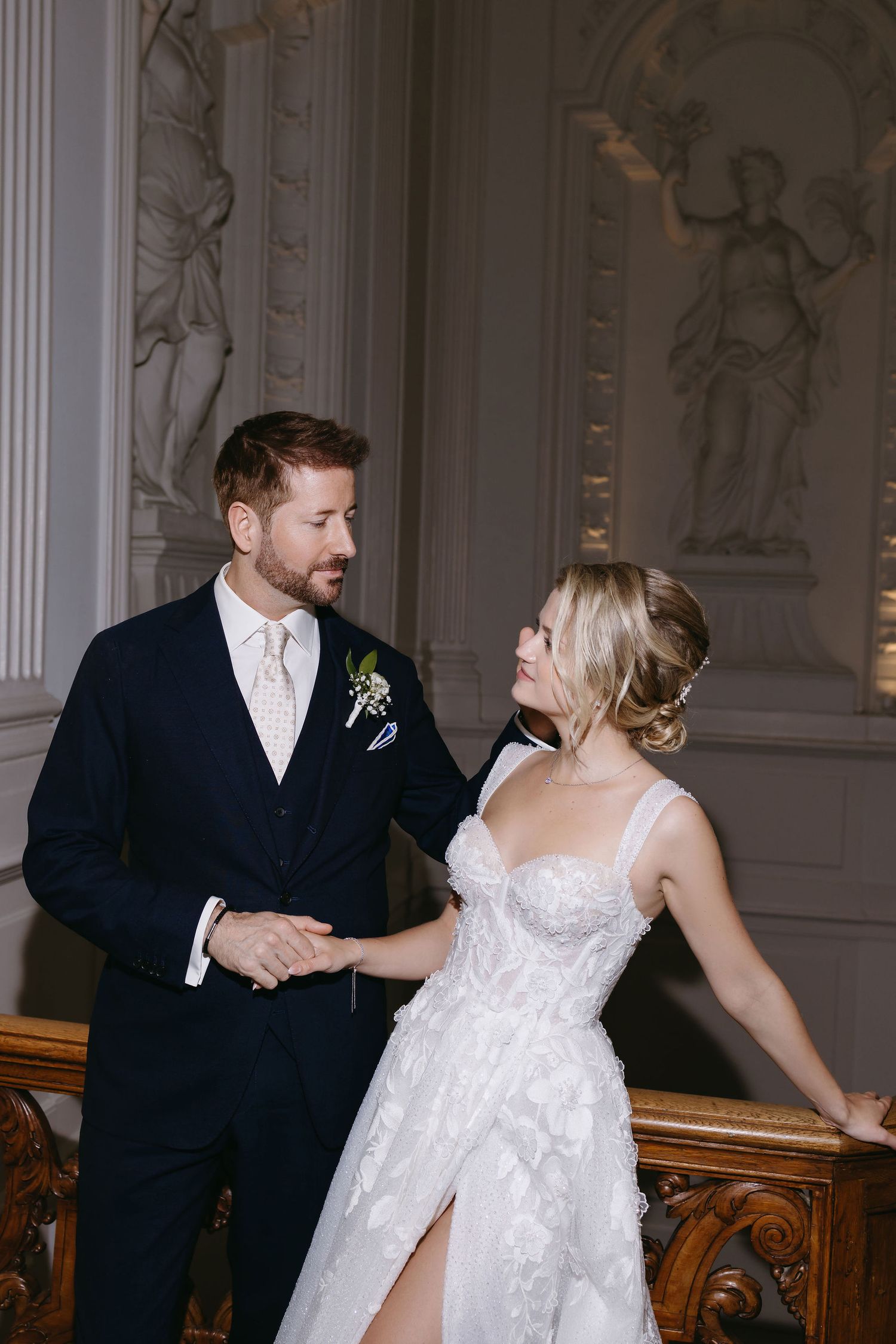 Elegant wedding couple dances together in an ornate ballroom with classical white pillars and decorative moldings.