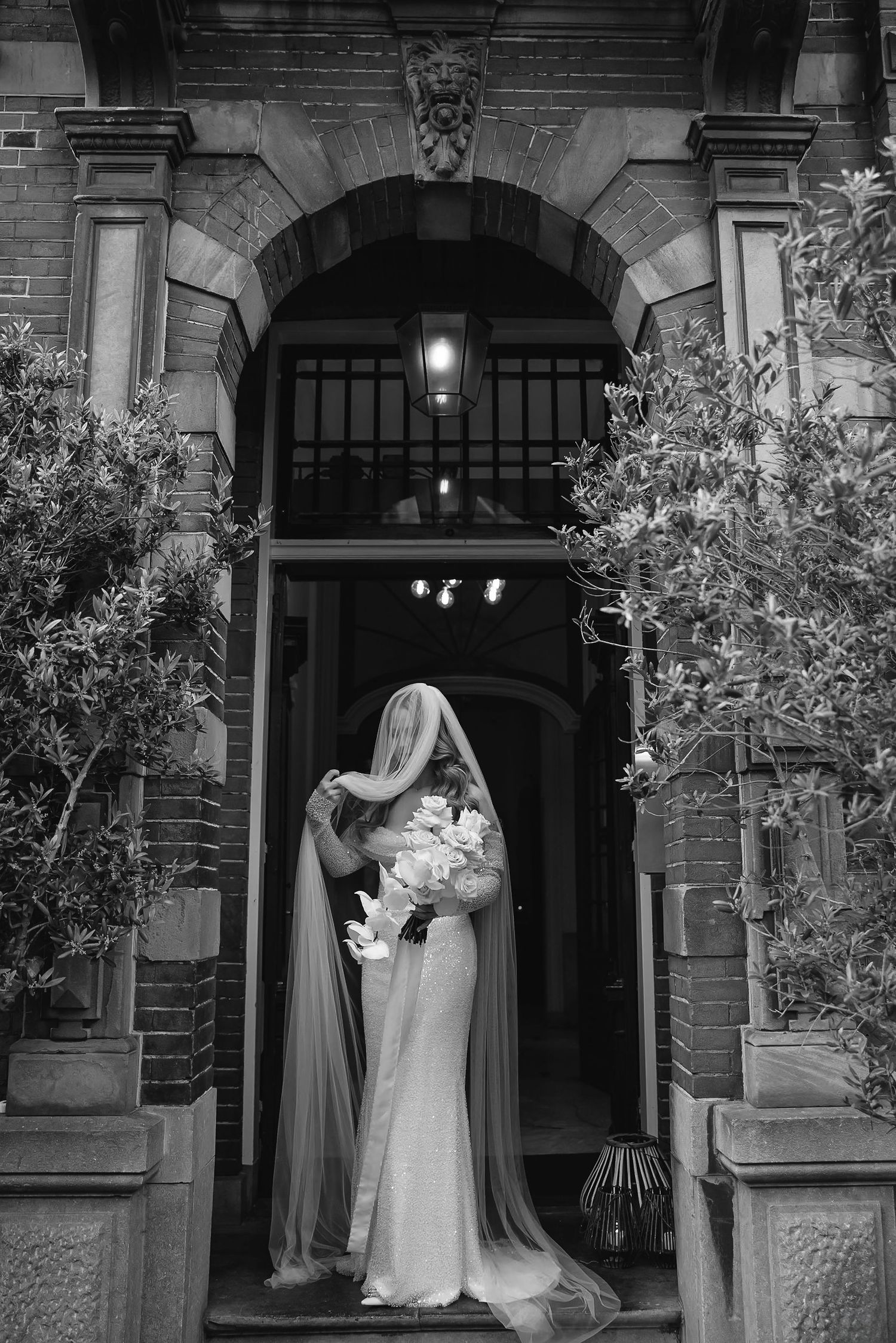 A ghostly figure dressed in white stands outside a dimly lit historic brick building entrance at night.