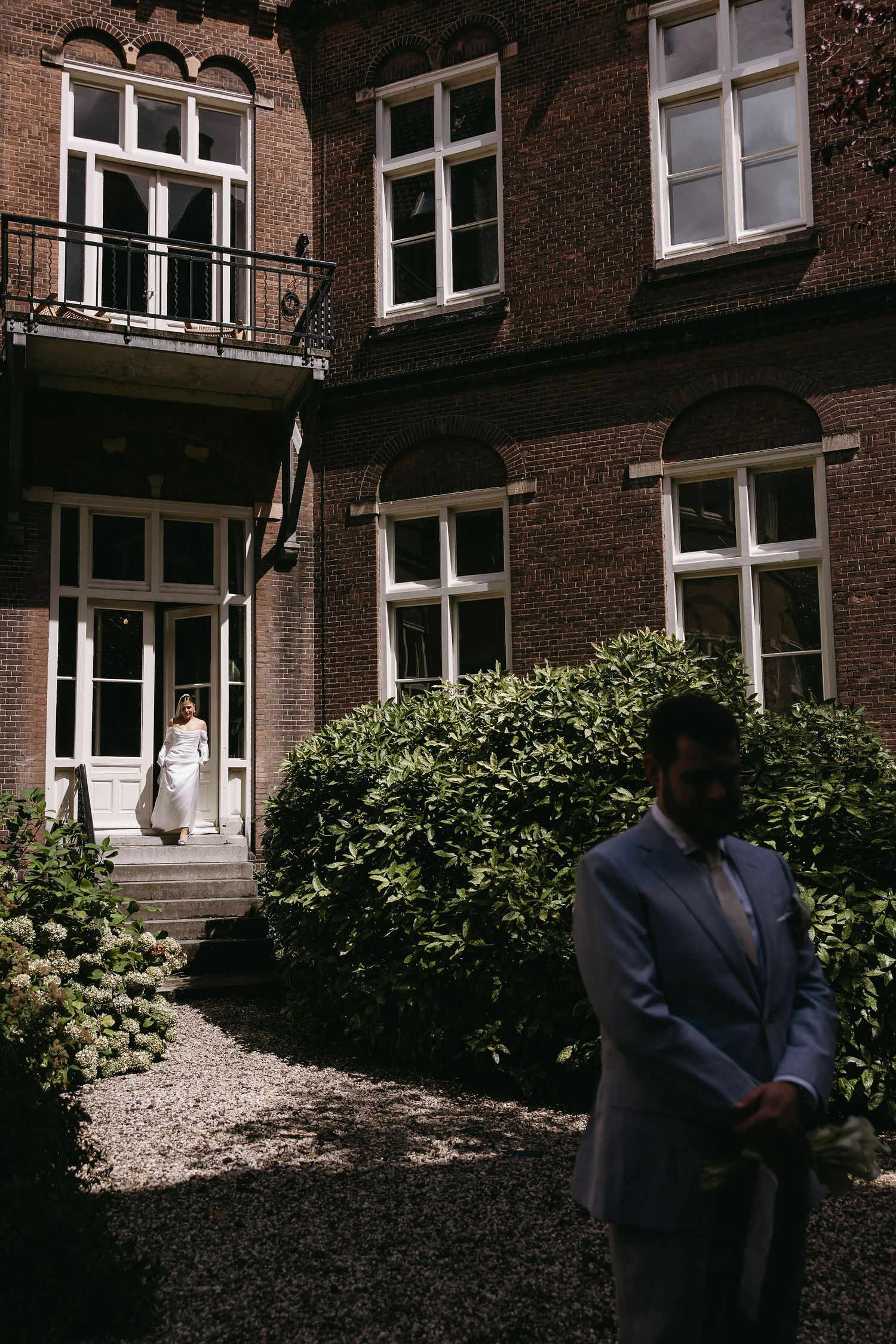 Classic brick building exterior with wedding party in formal attire and garden landscaping.