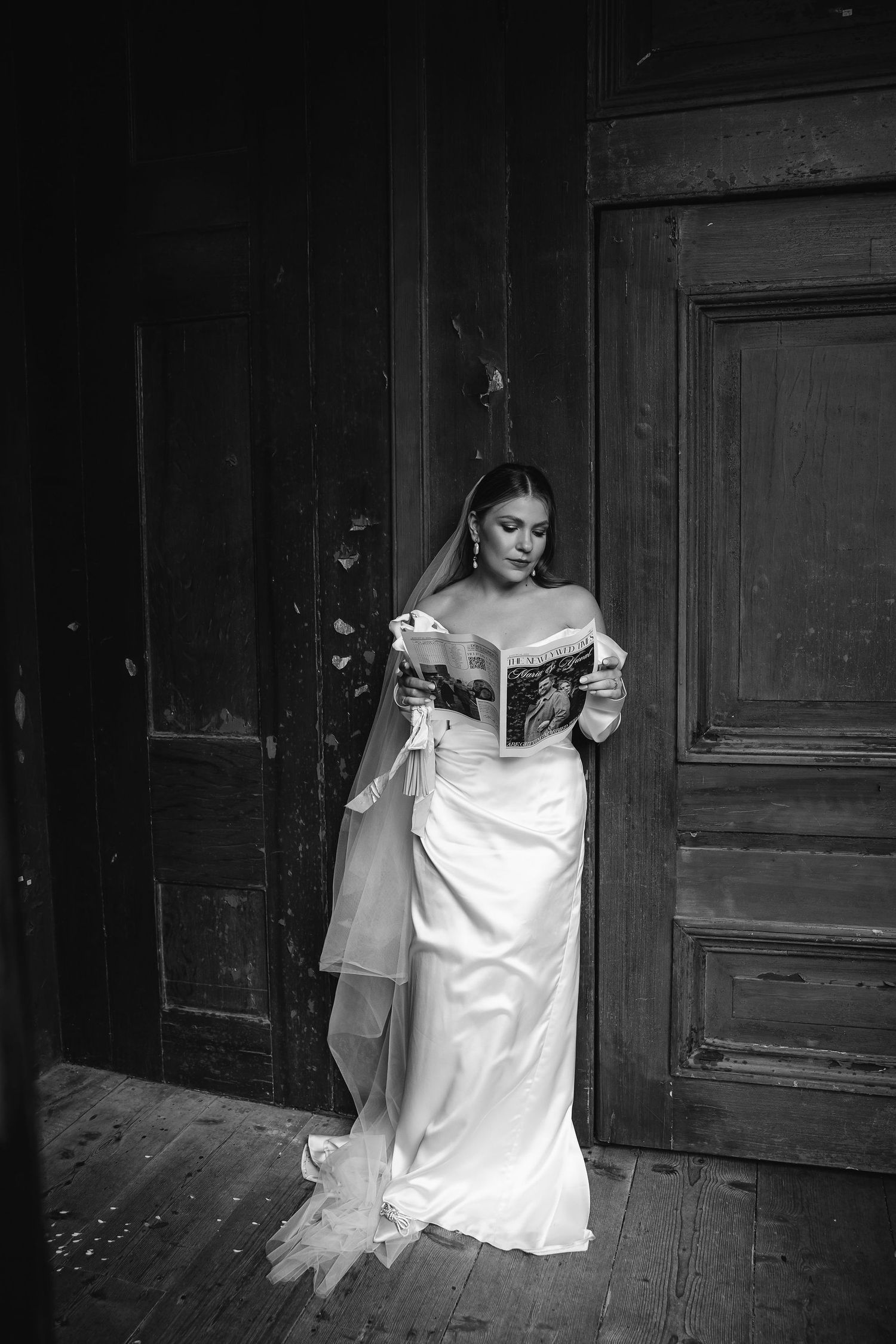 Black and white image of bride in flowing white dress near vintage wooden doors.