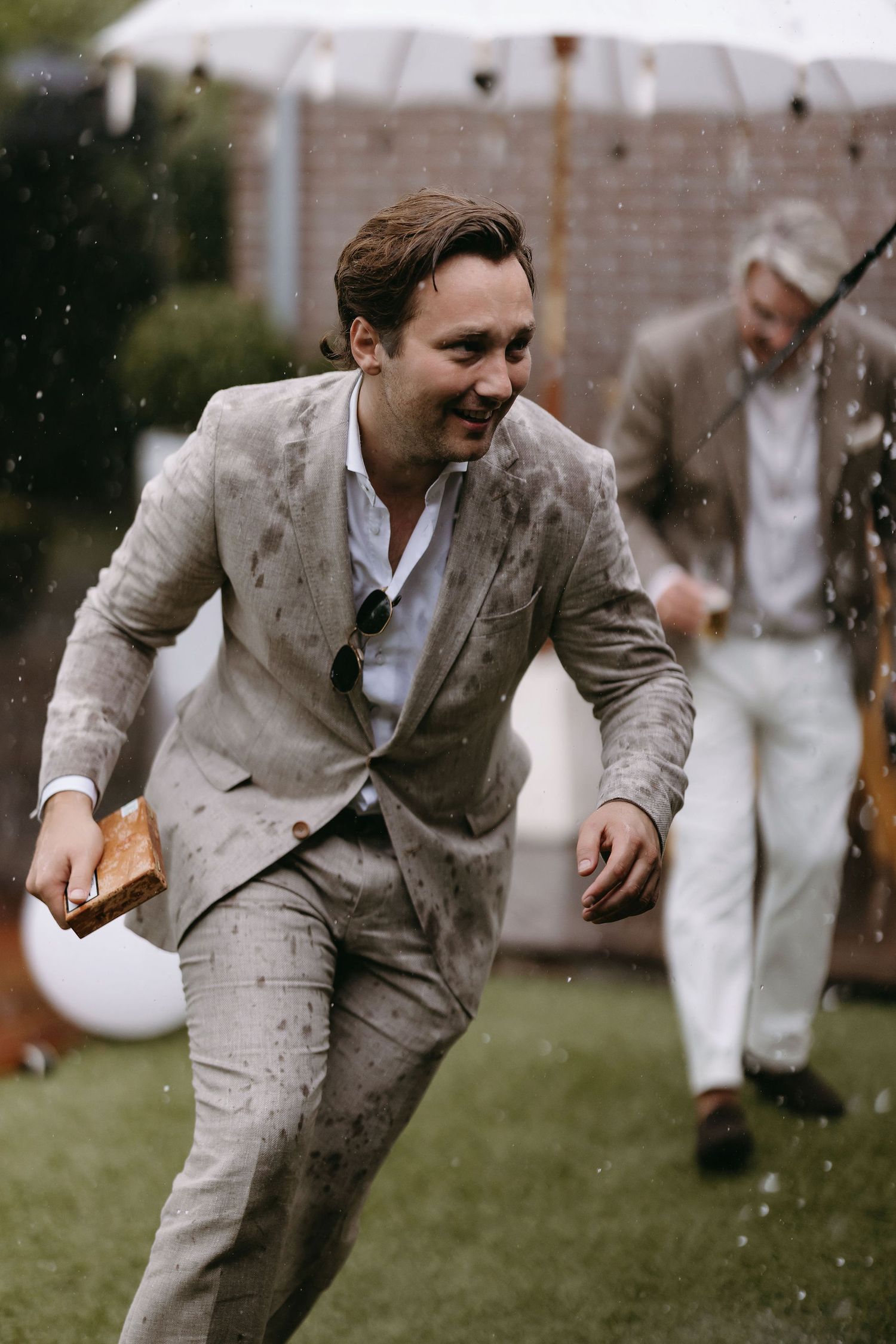 Person in light suit laughing while running in the rain during outdoor event.