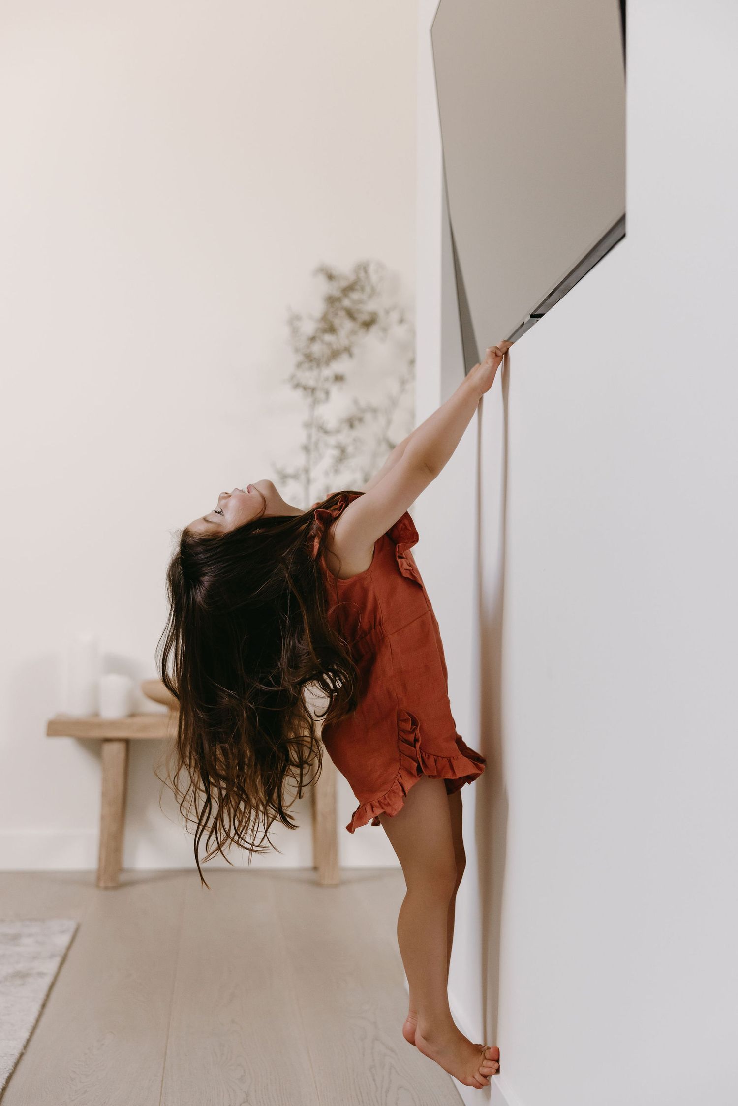 Small child in a red dress plays energetically against a white wall, demonstrating youthful joy and movement.