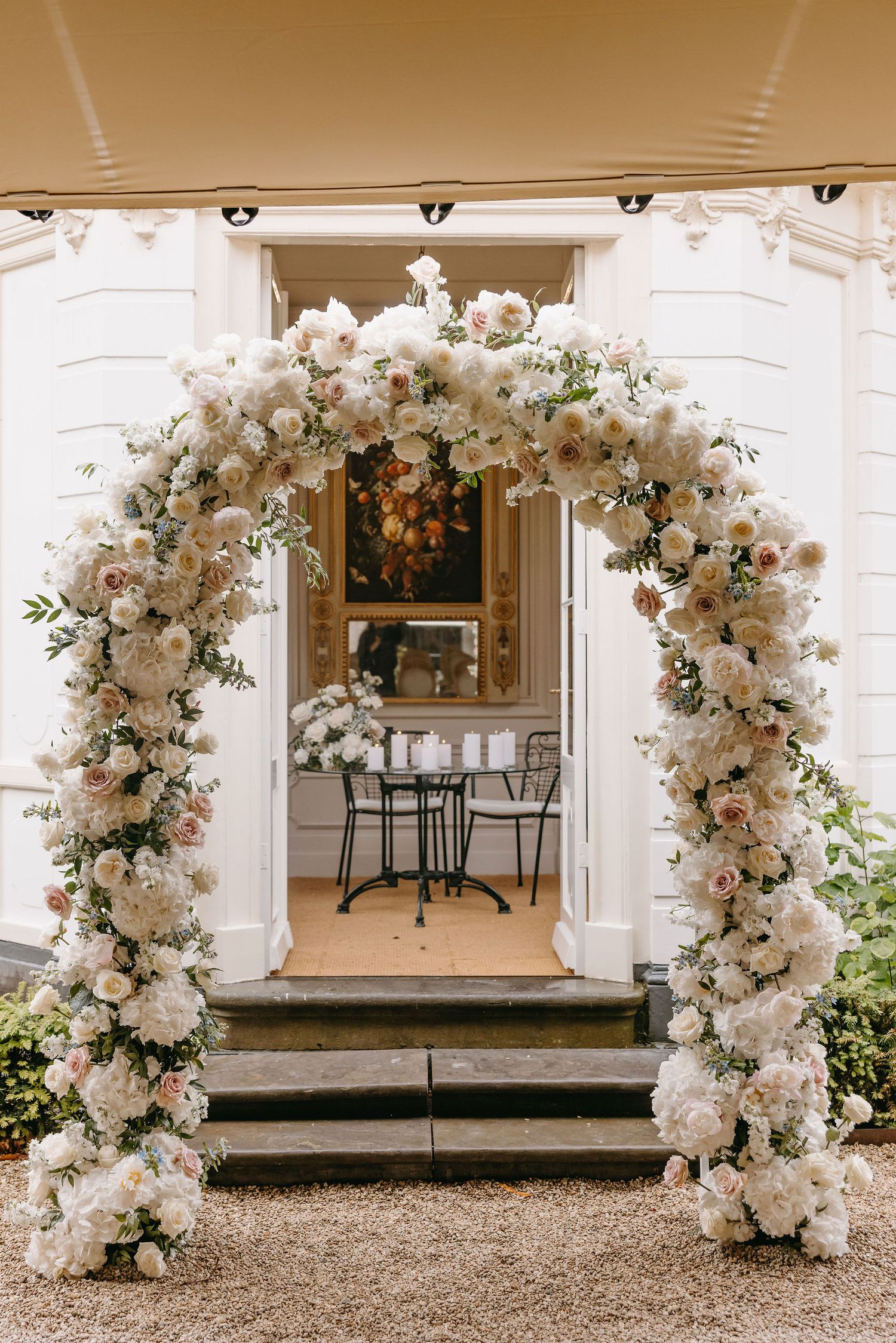 Stunning white floral arch with roses and greenery framing an elegant doorway entrance.