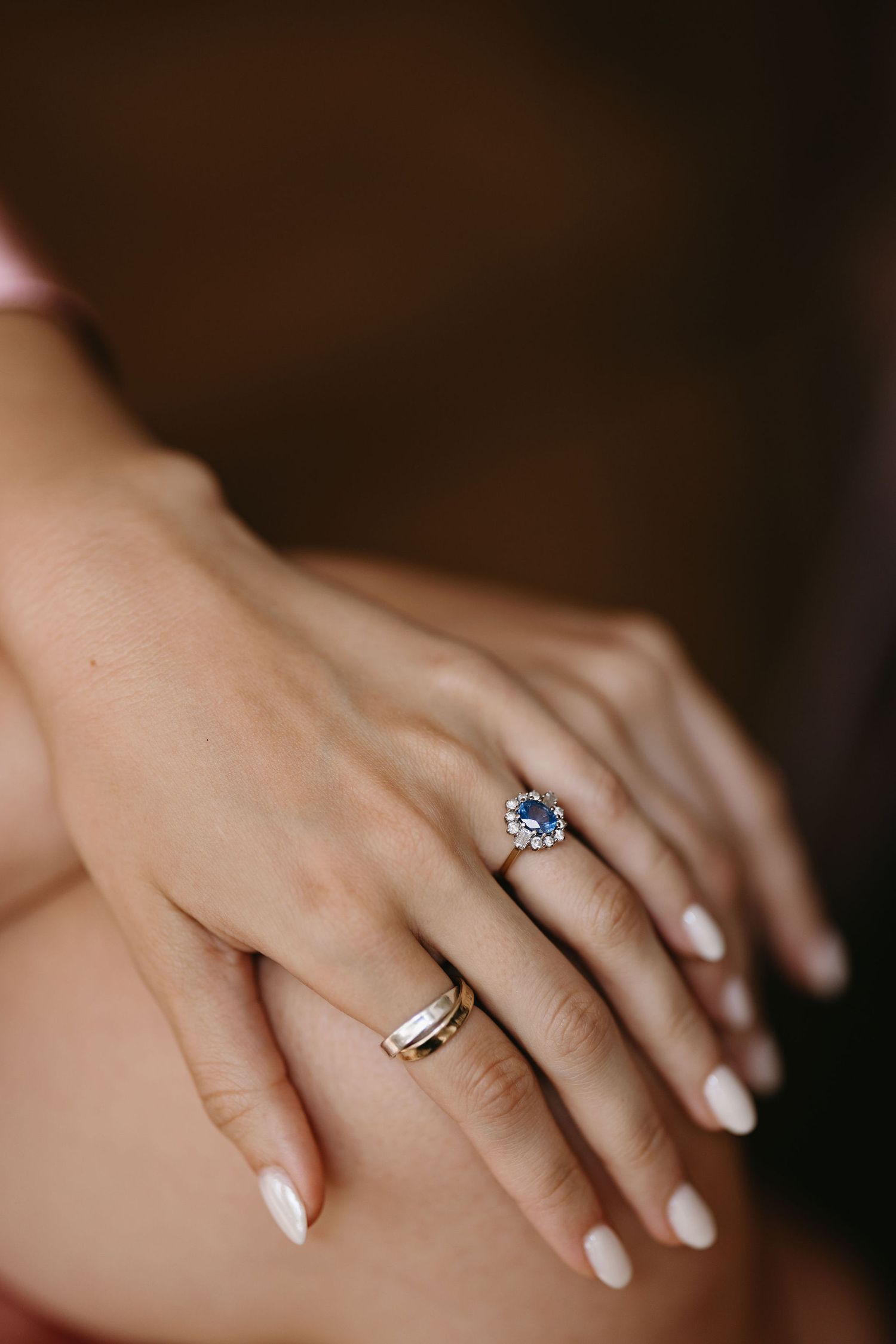 Close-up details of delicate wedding rings and manicured hands on a dark background.