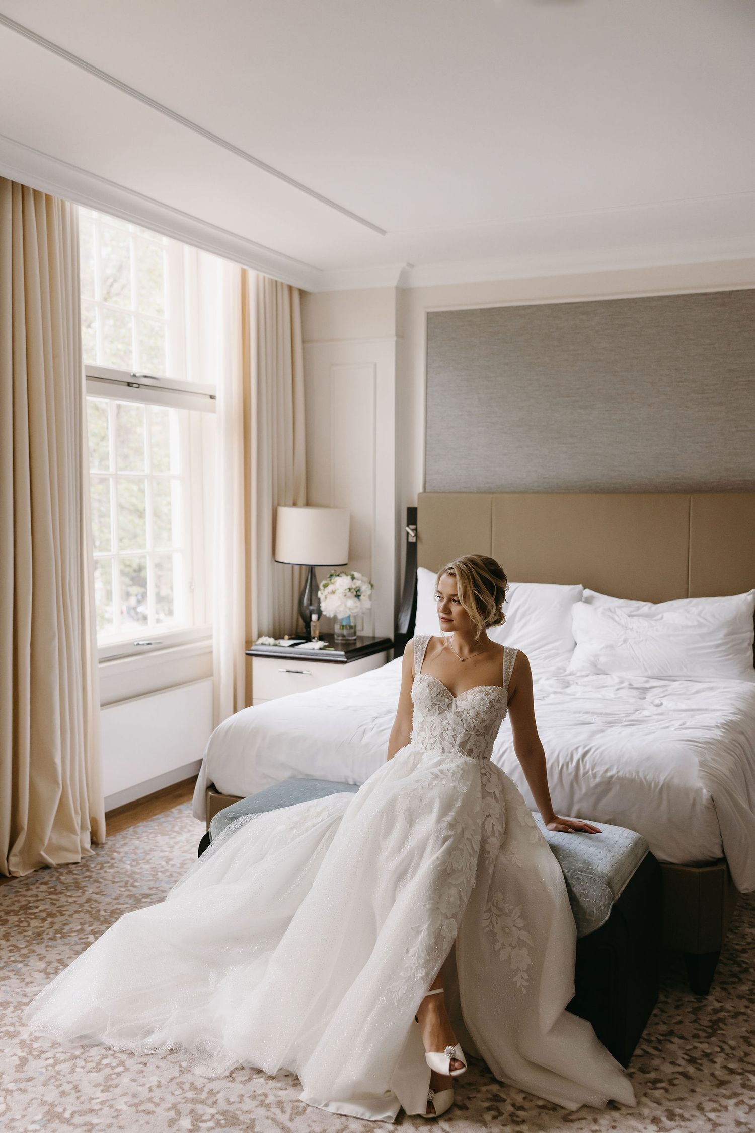 A flowing white wedding gown elegantly draped across a modern hotel room bed.