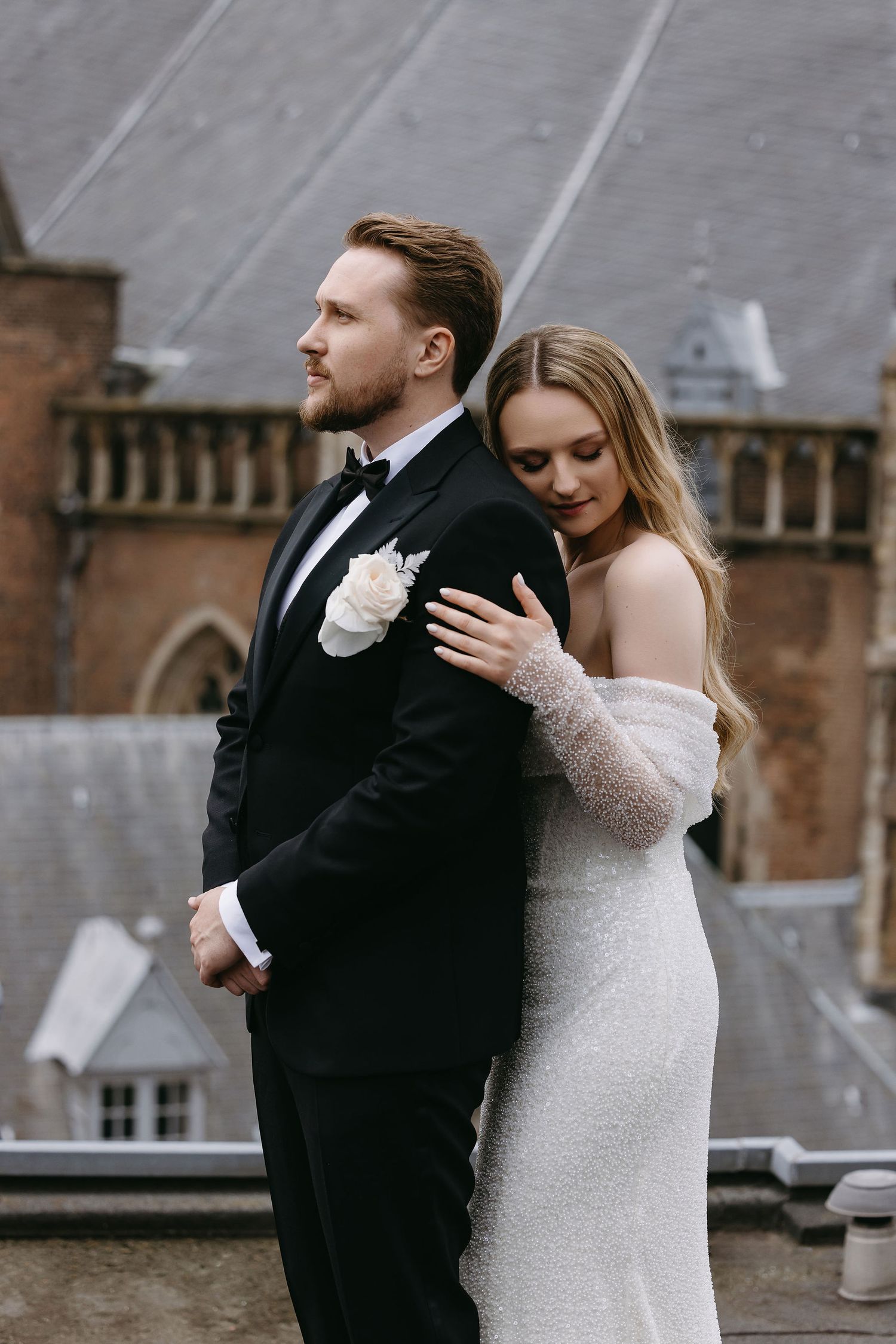 Romantic wedding portrait on a rooftop with bride in sparkly dress embracing groom in black tuxedo.