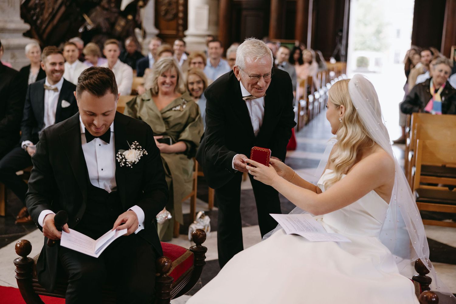 Wedding ceremony in grand church interior with guests seated in wooden pews.