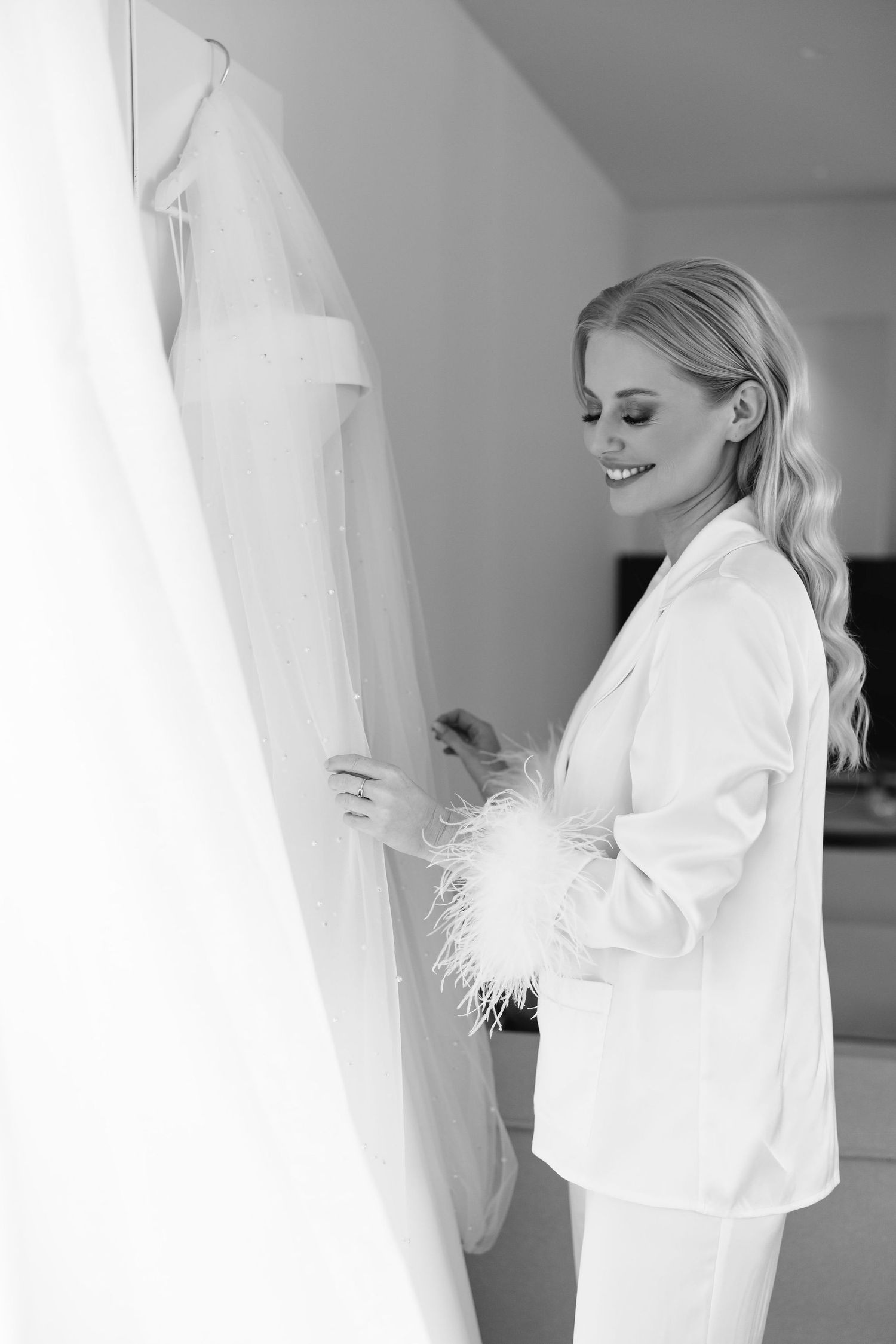 A person in a white robe admires a wedding dress hanging on display.