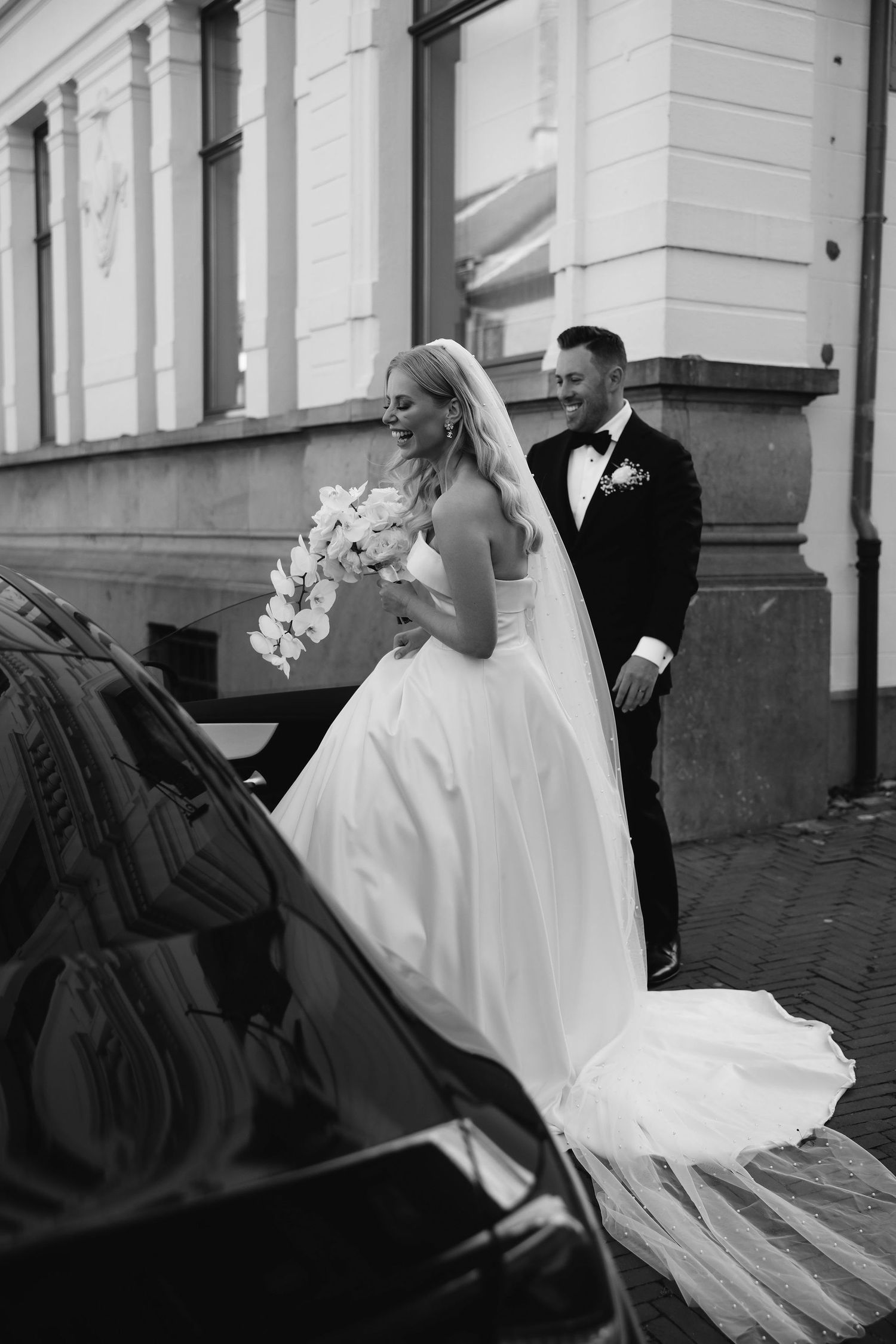 Black and white photo of newlyweds next to a vintage car.