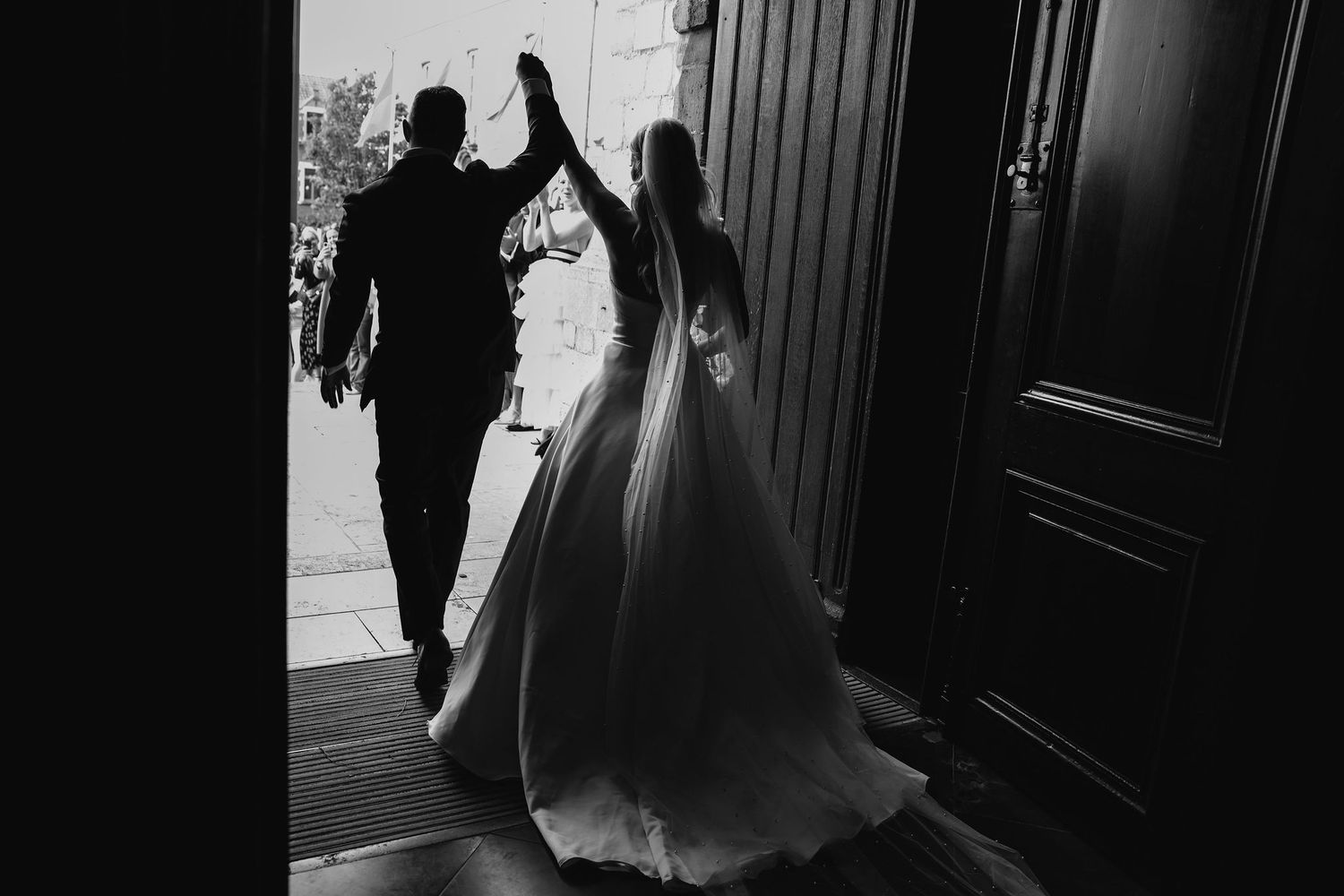 Silhouette of a couple in wedding attire walking hand-in-hand towards a doorway.