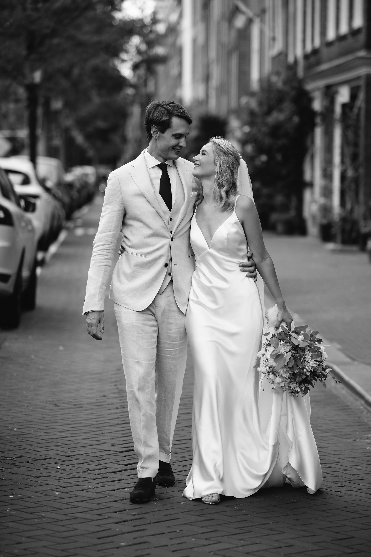 Couple in white formal attire walking together on a cobblestone street.