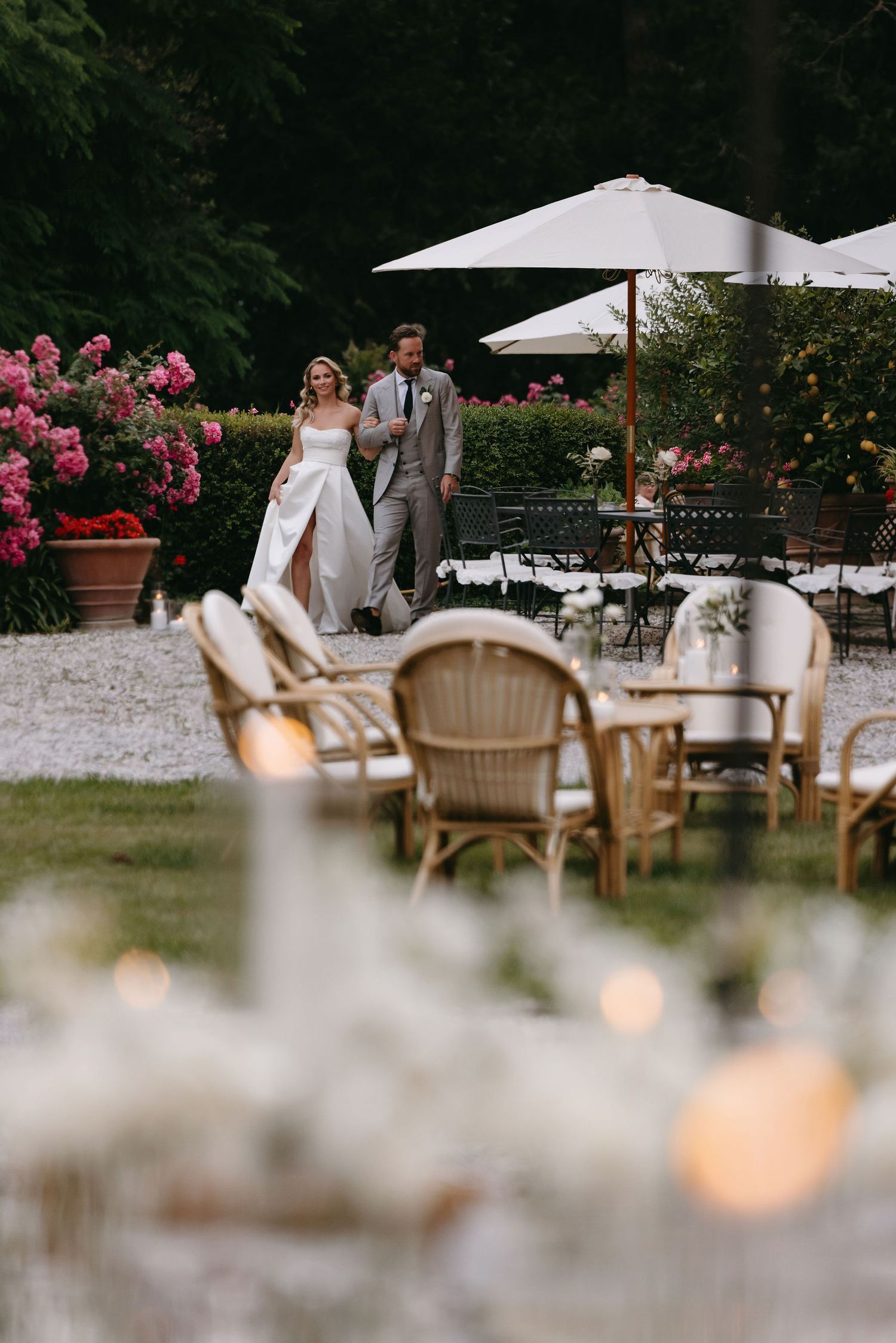 Elegant outdoor wedding reception area with rattan chairs, umbrellas, and blooming rose gardens.