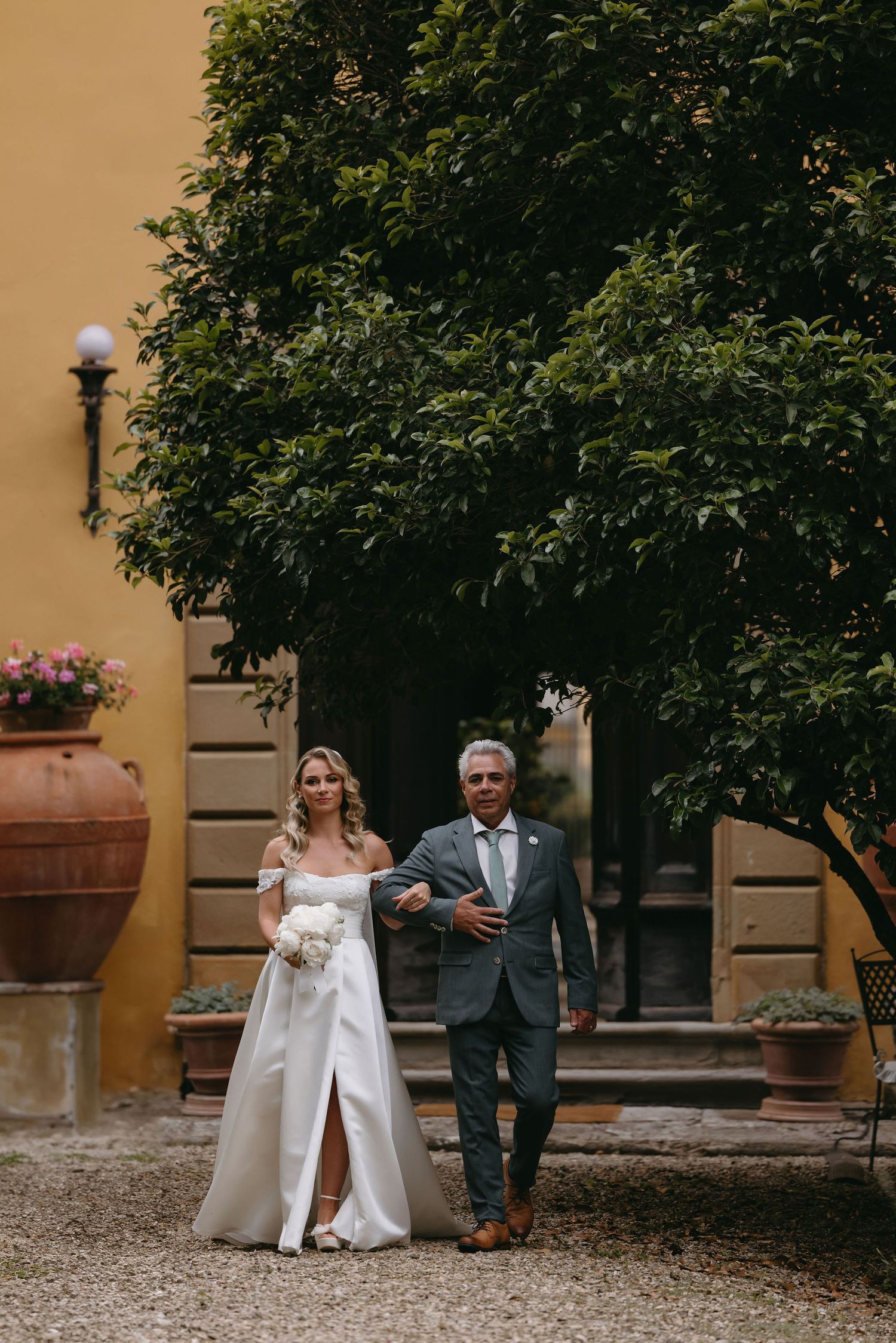 A couple walking arm in arm through a garden courtyard at an Italian villa.