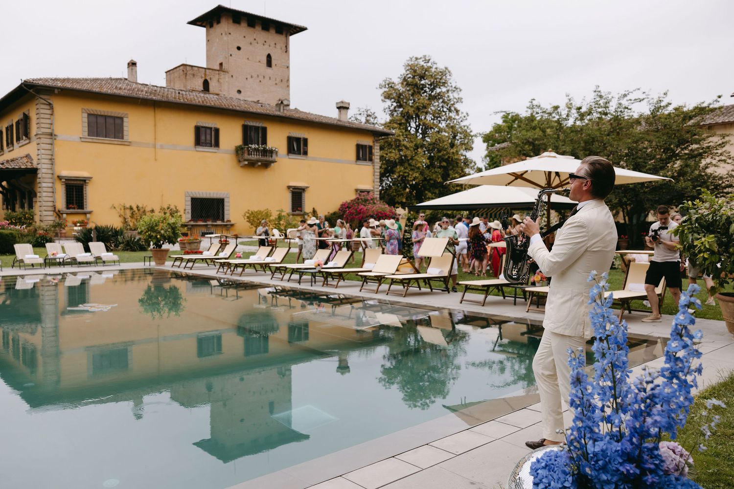 Poolside wedding venue at a Tuscan villa with guests gathering under umbrellas.