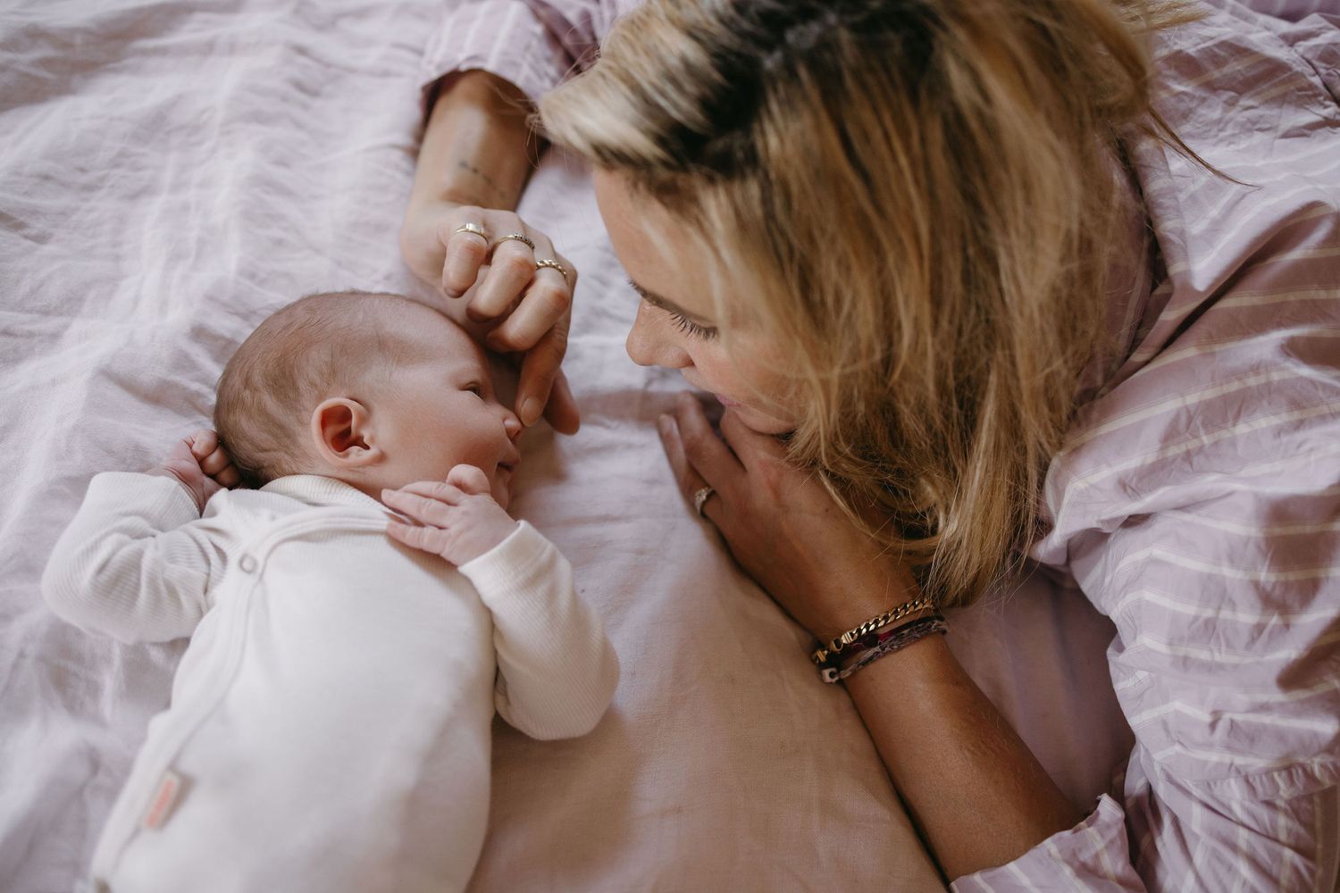 An intimate close-up of a parent and newborn lying together on white bedding.
