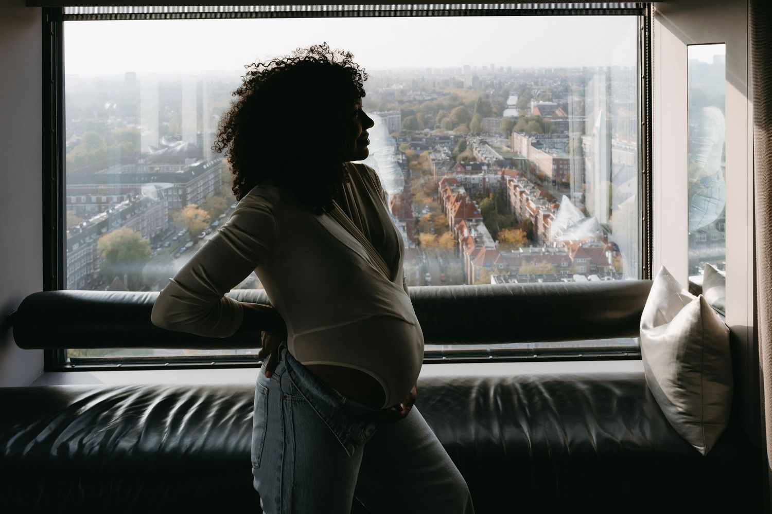 Person looks out large window at cityscape view while reclining on window seat.