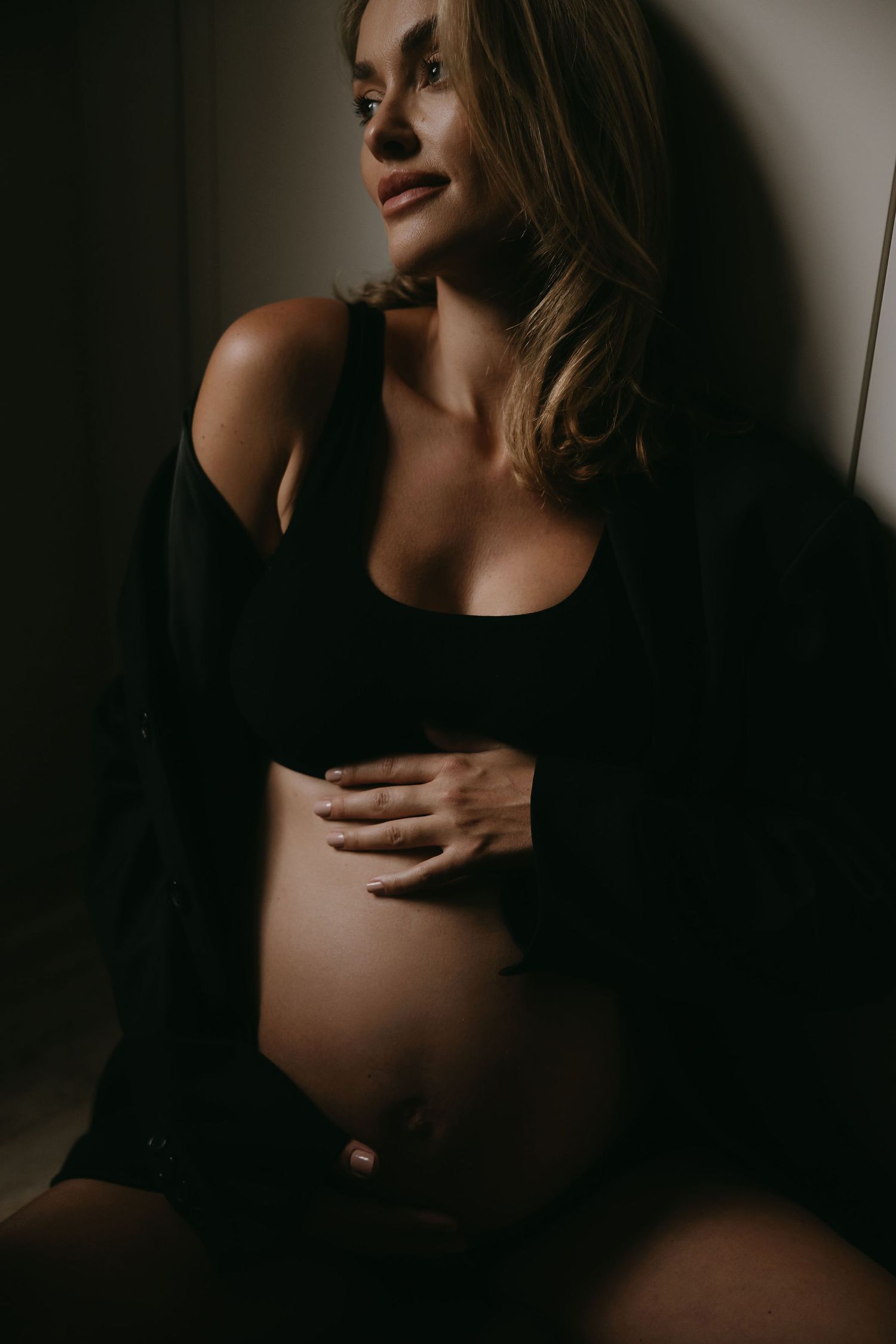 Moody maternity portrait with subject wearing black sweater against dark background.