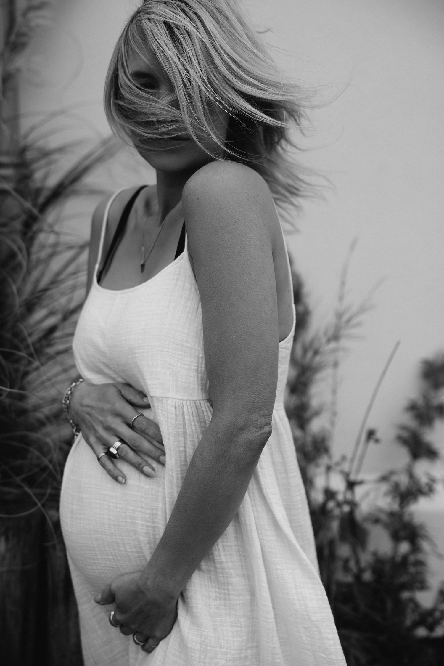 Black and white outdoor maternity photo in flowing white dress with windswept hair.