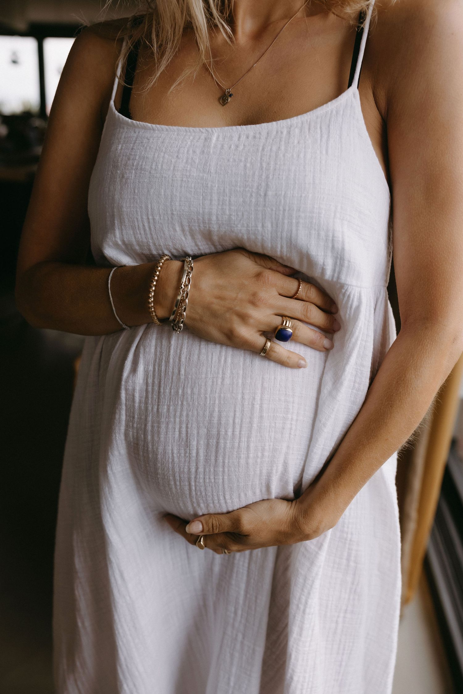 Close-up shots of hands gently cradling a pregnant belly in white dress.
