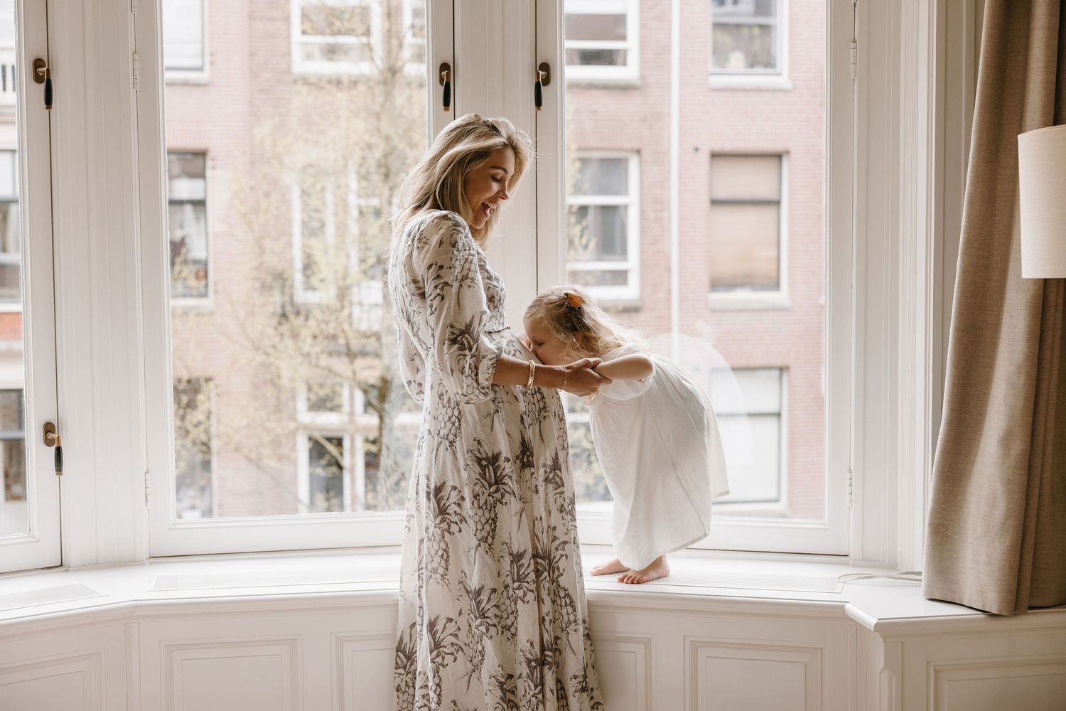 Mother and daughter share sweet moment by bright bay window.