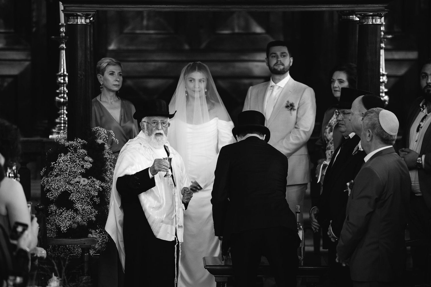 Dark silhouettes of wedding guests gathered at an indoor ceremony.